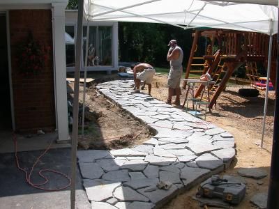 A group of men are working on a stone walkway in front of a playground.