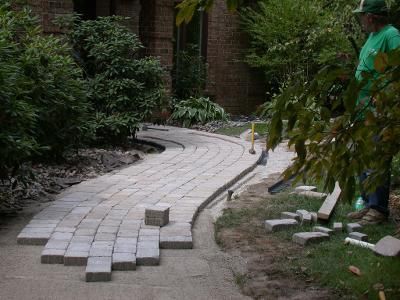 A man in a green shirt is standing next to a brick walkway being built.