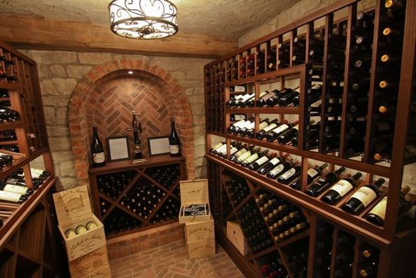 Wine cellar with brick walls, arched alcove, and wooden wine racks filled with bottles.