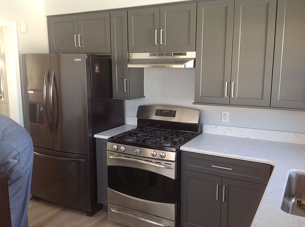 Gray kitchen cabinets with stainless steel appliances and white countertops.