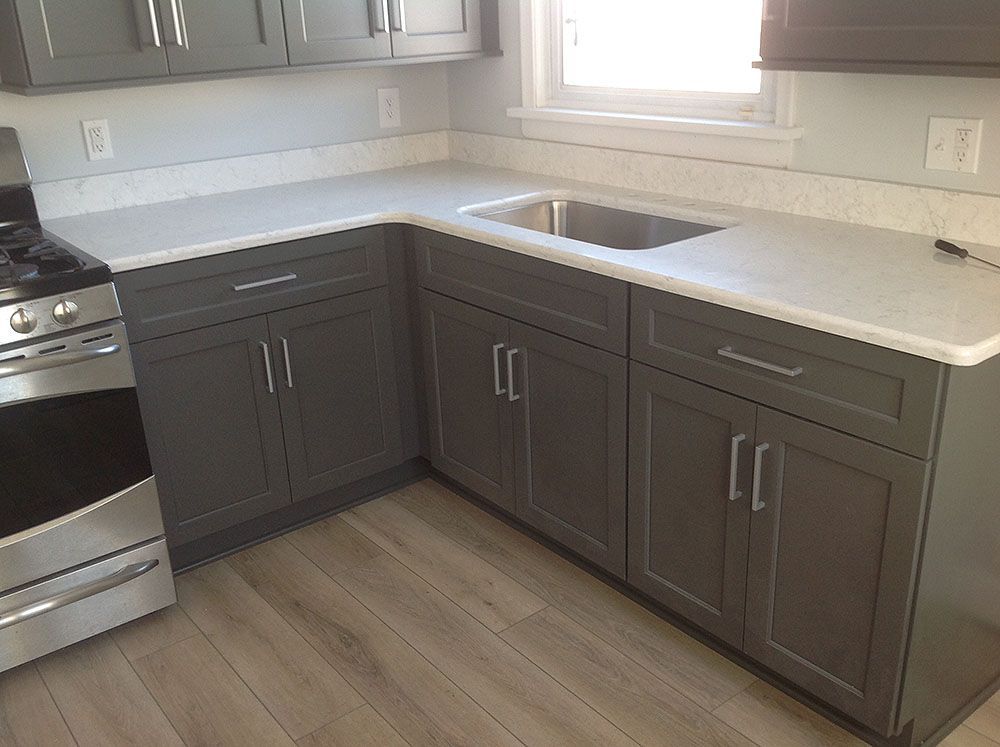 Gray kitchen cabinets with white countertops and stainless steel appliances; wood floor.
