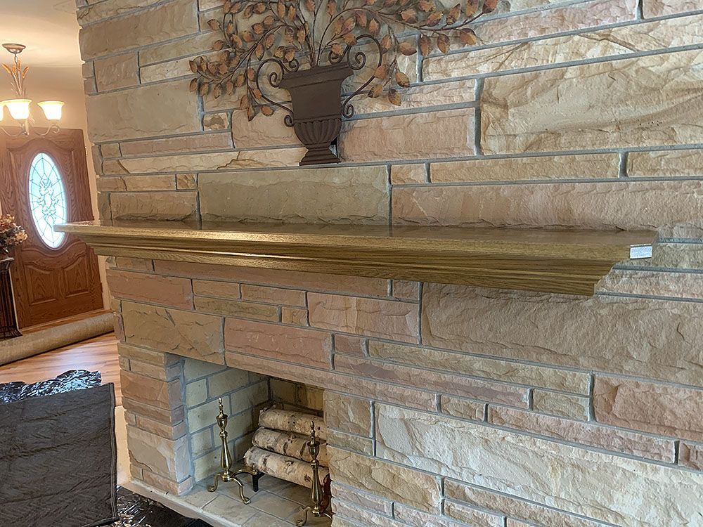 Fireplace with tan stone, wooden mantel, and decorative metal wall art.