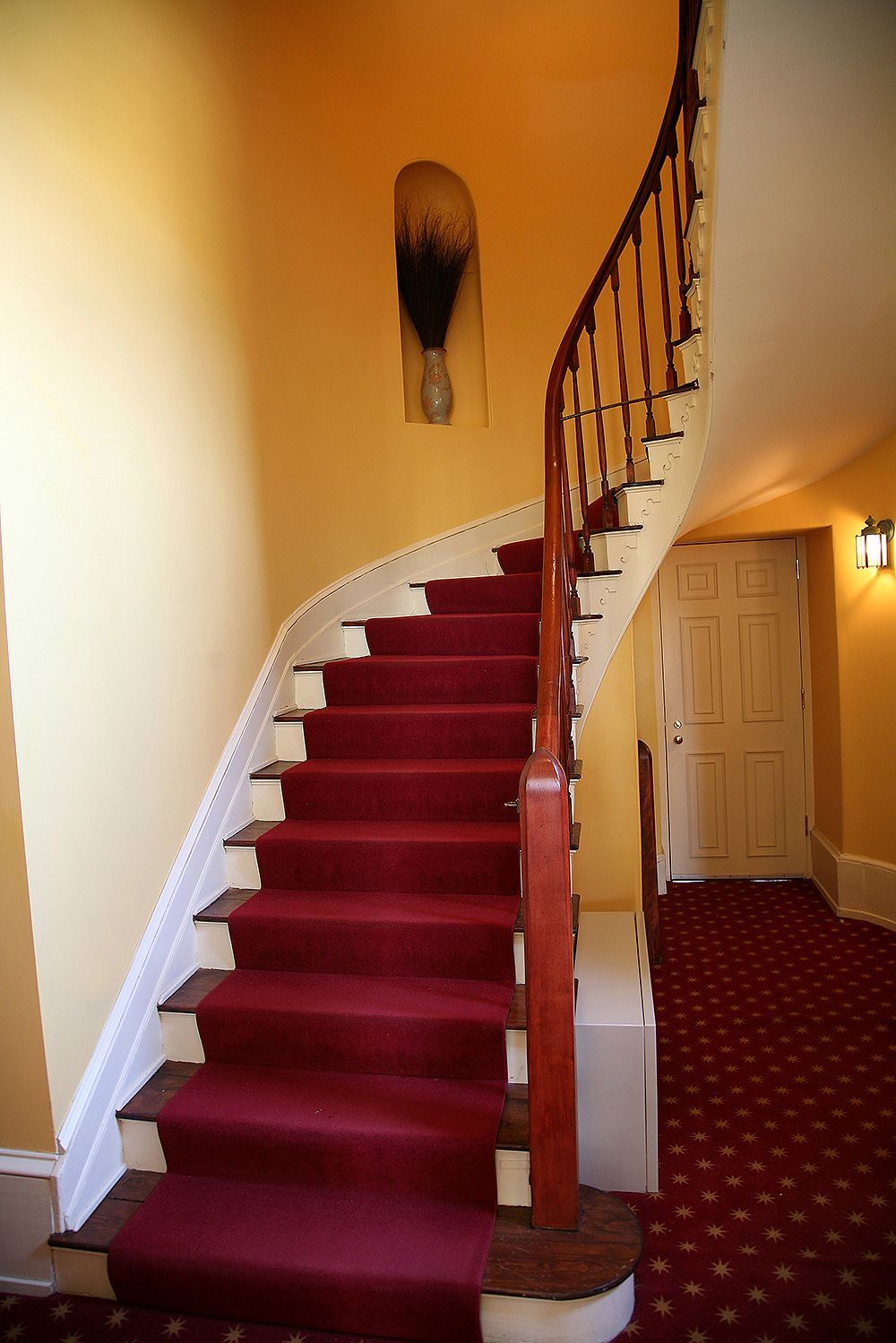 Curving staircase with red carpet, wooden handrail, and yellow walls.