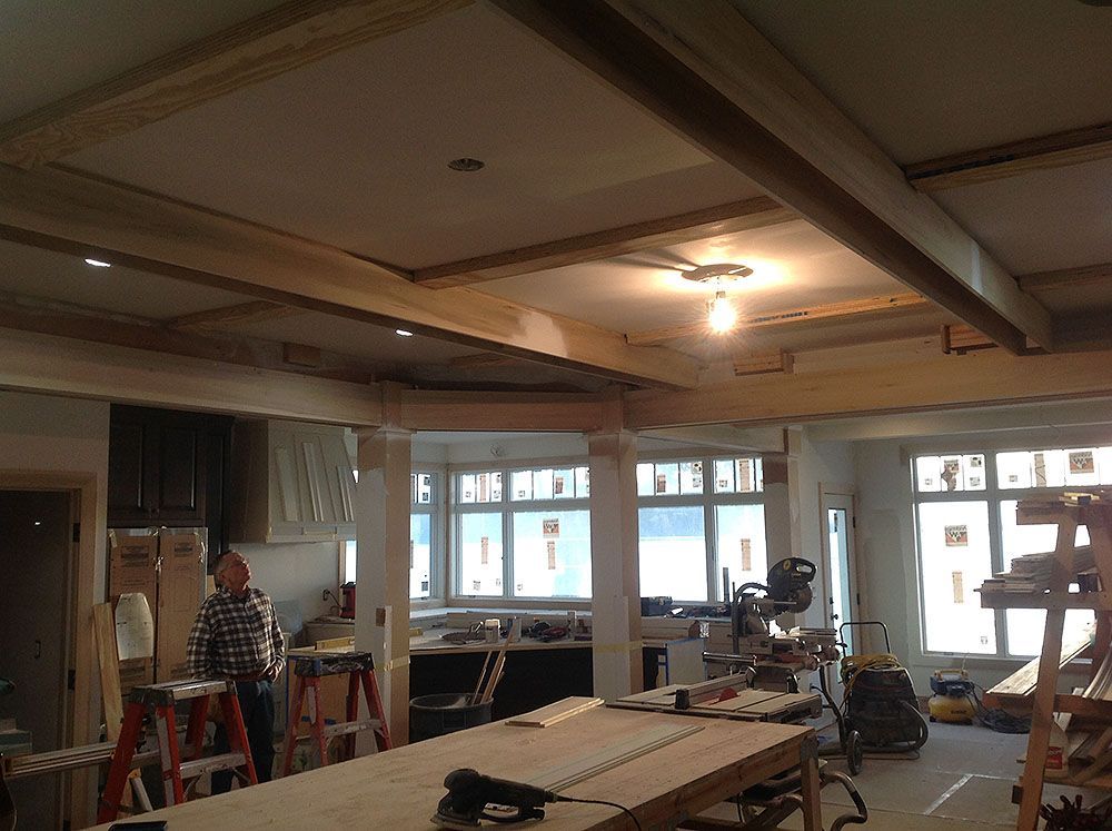 Construction site with a man in the foreground. Wooden beams on the ceiling and work table in the middle.