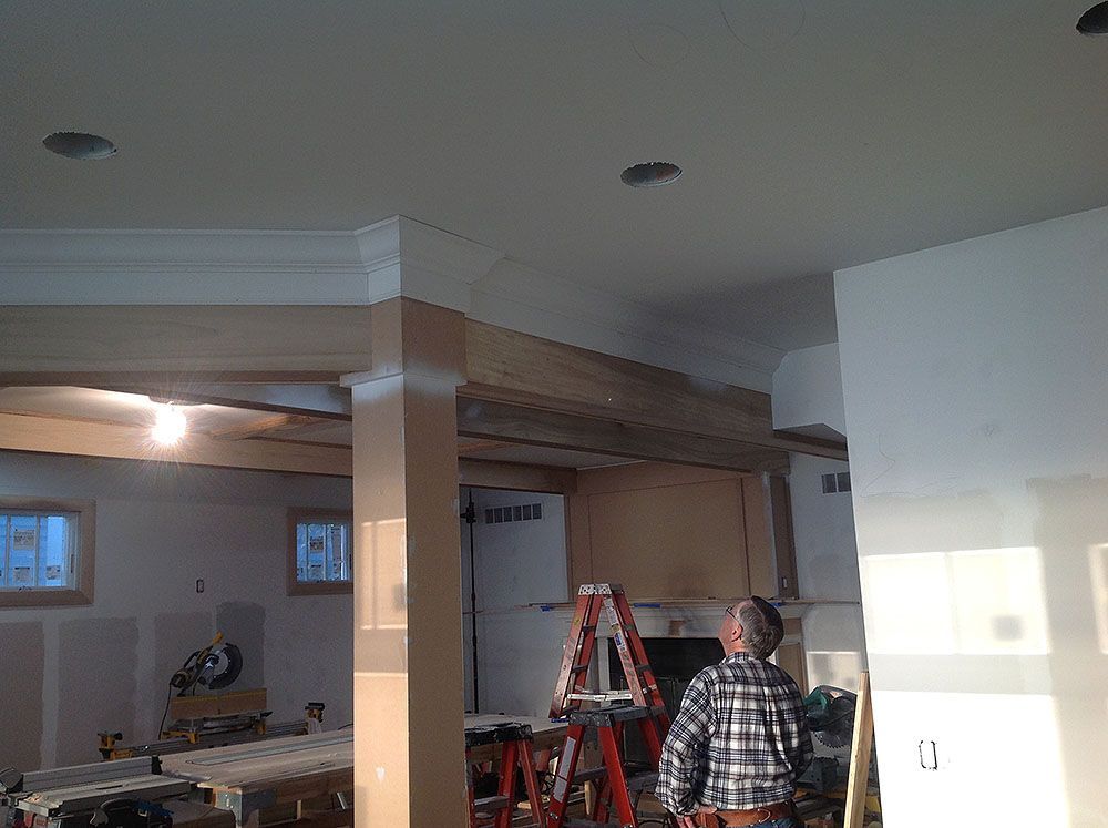 Man looking up at construction; interior room with crown molding, ladder, and tools.