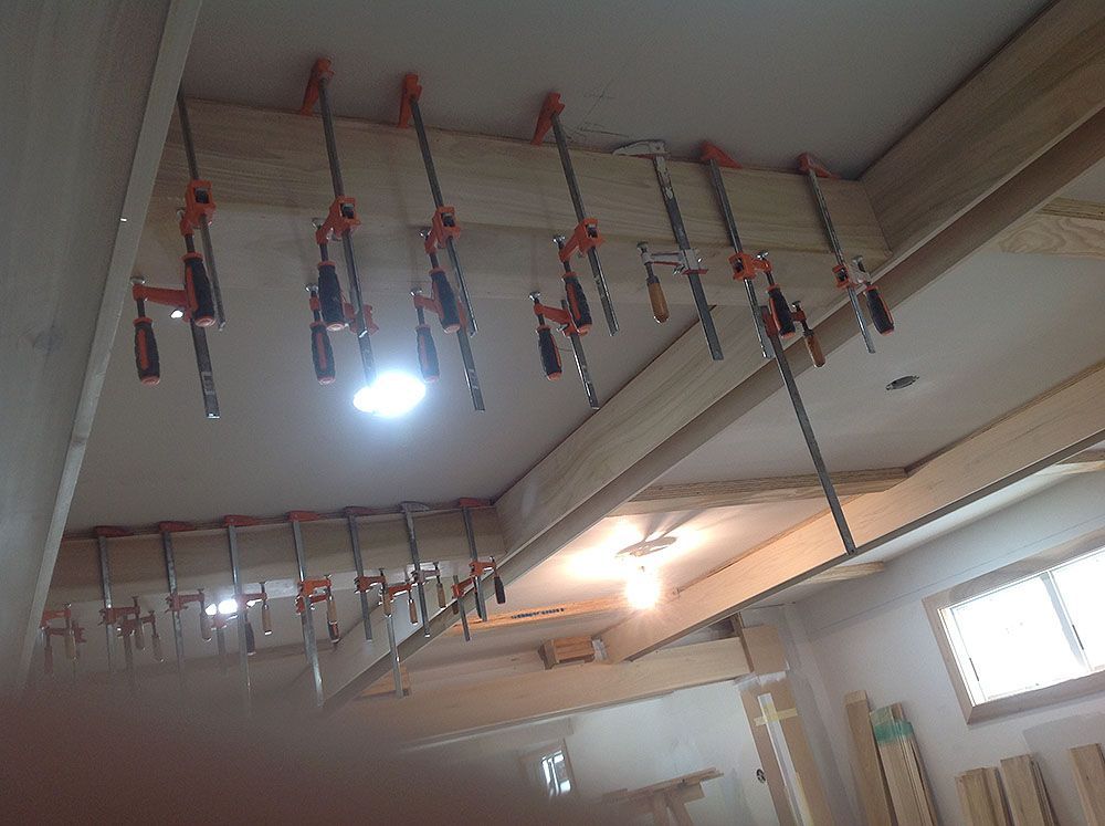 Wooden boards clamped to a ceiling with orange and black clamps in a workshop.