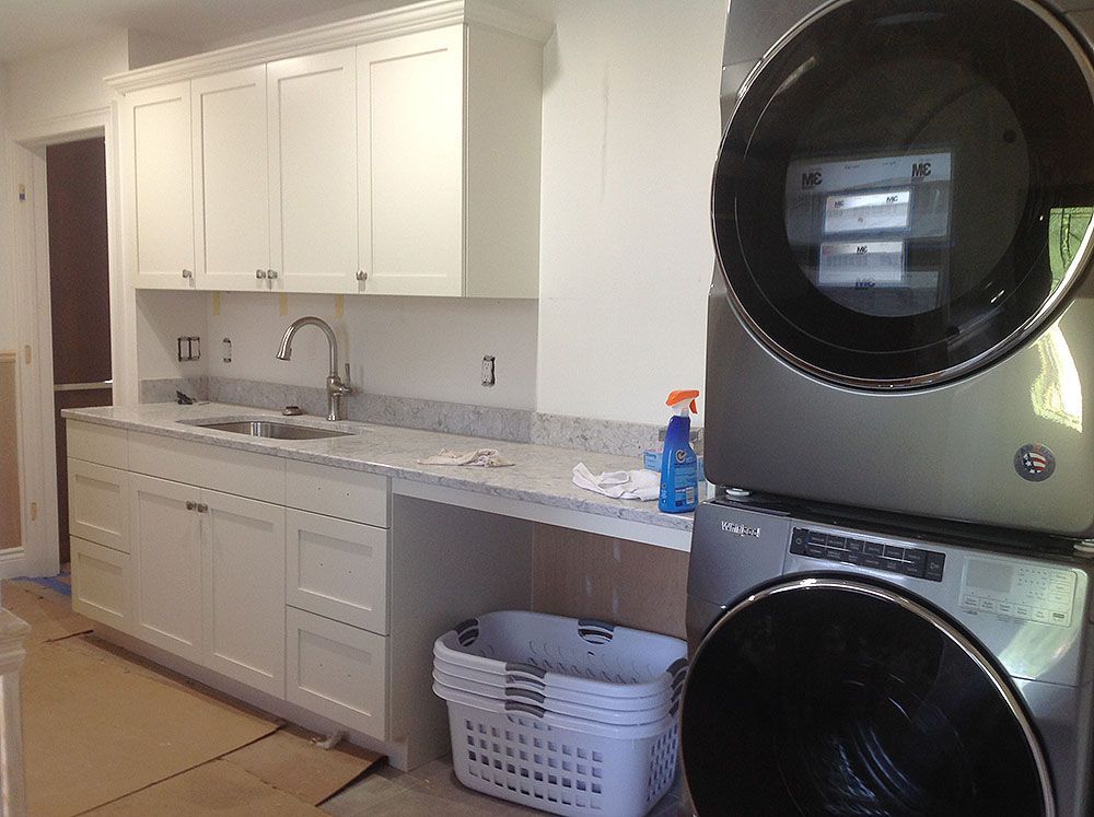 Laundry room with white cabinets, granite countertops, stacked washer/dryer, and a sink.