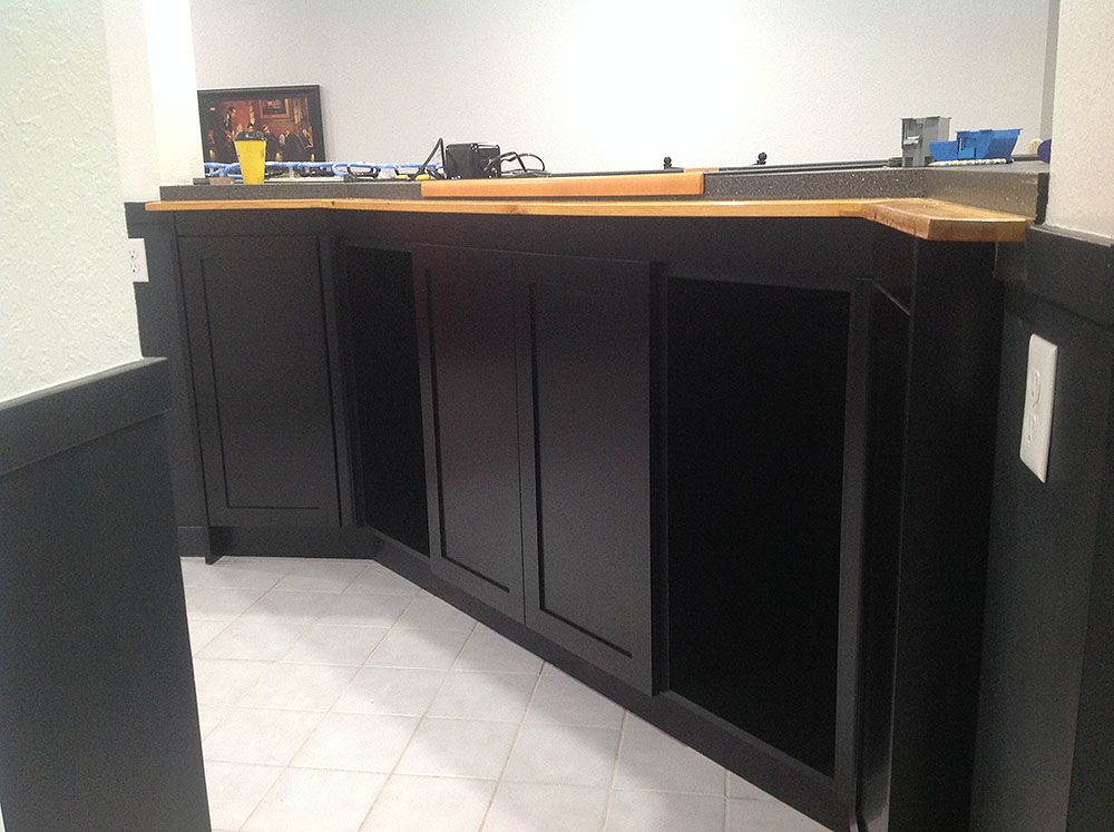 Black bar with light wood countertop in room with white tile floor and walls.