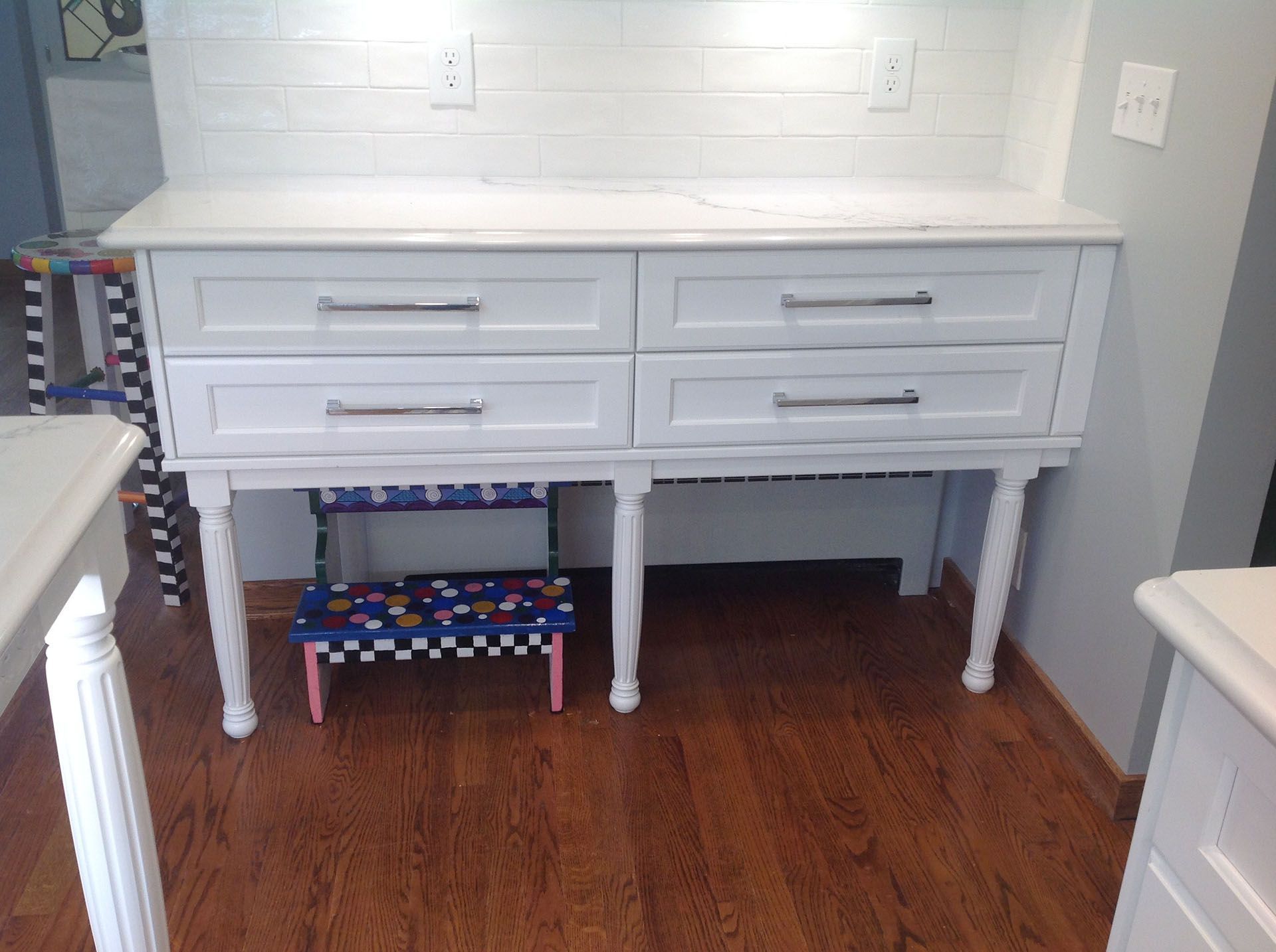 White dresser with drawers under a white countertop, with a decorative step stool in front.