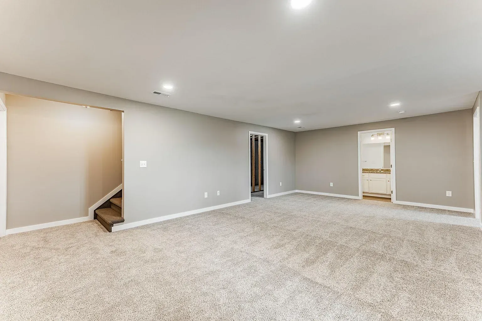An empty basement with a staircase and a carpeted floor.