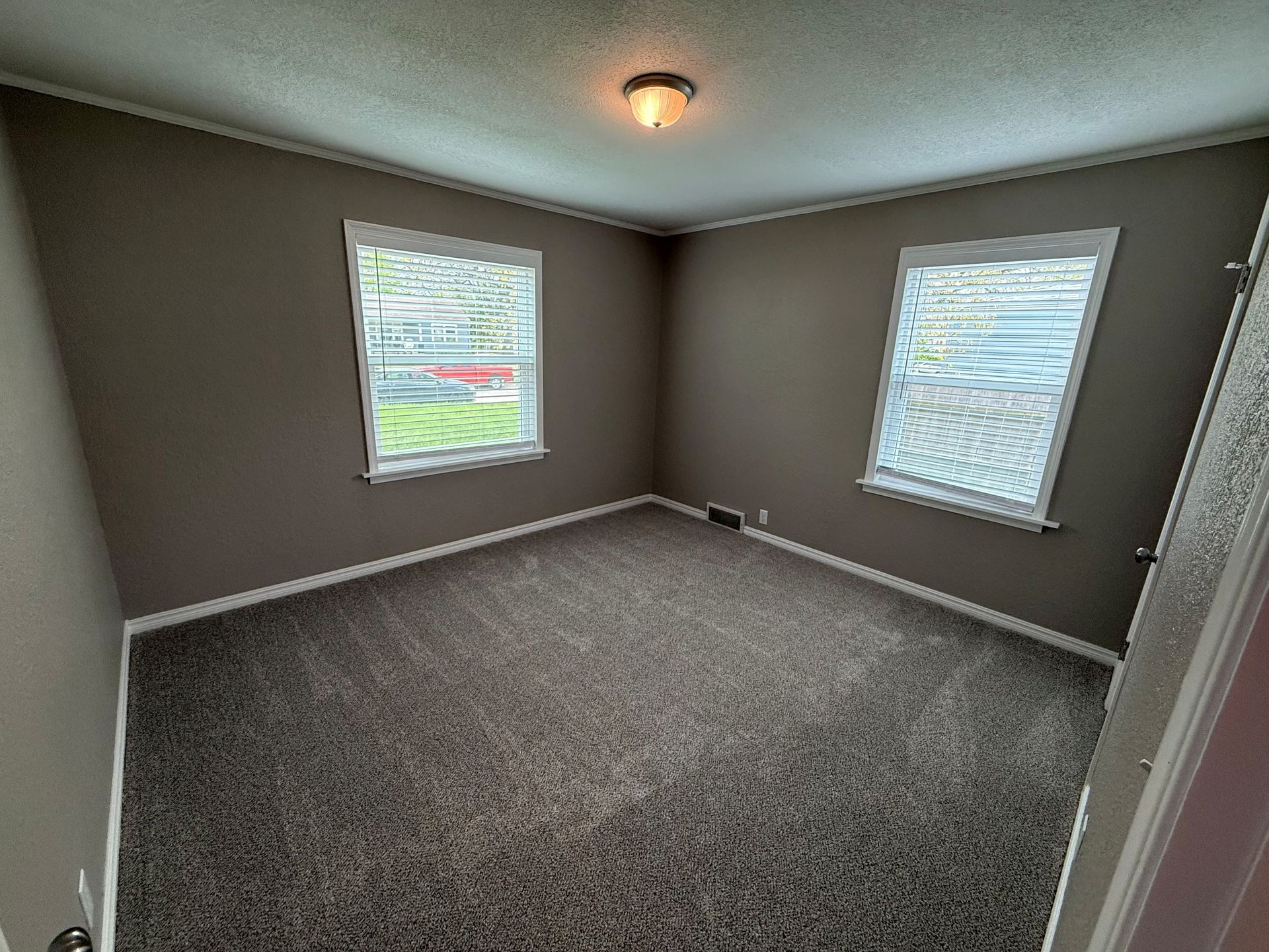 An empty bedroom with a carpeted floor and two windows.