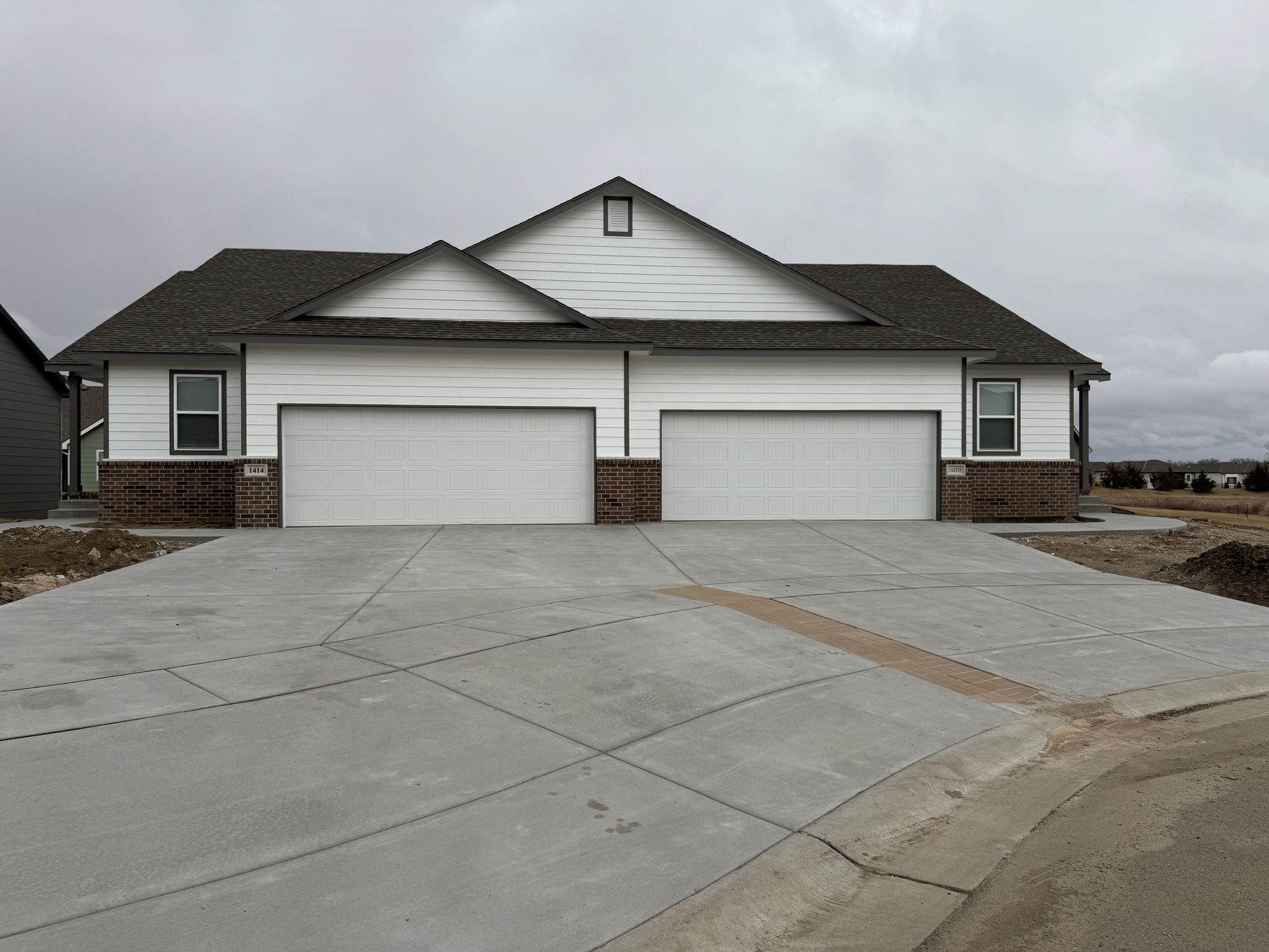A house with two garage doors and a concrete driveway in front of it.