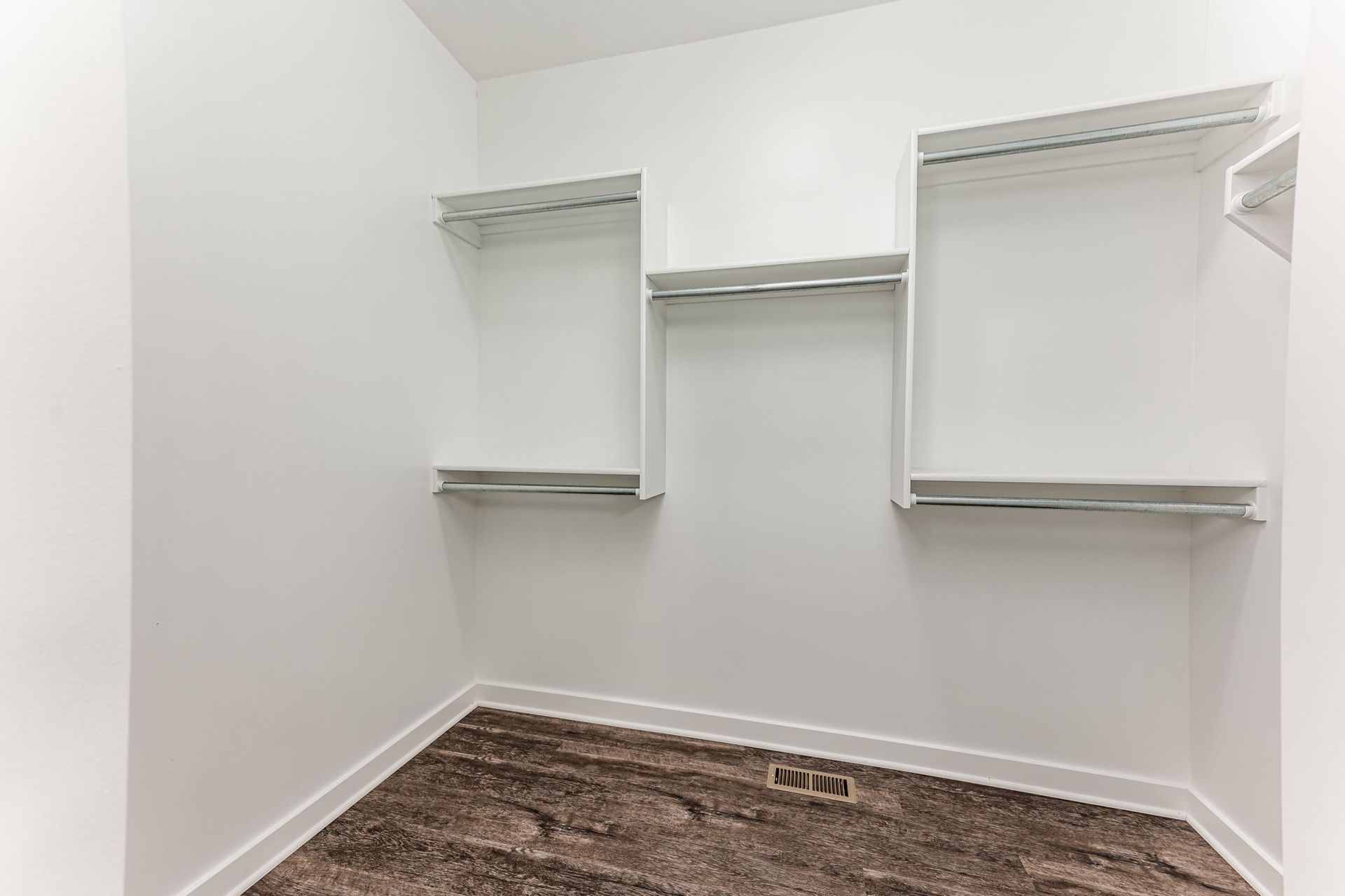 An empty walk in closet with white shelves and brown carpet.