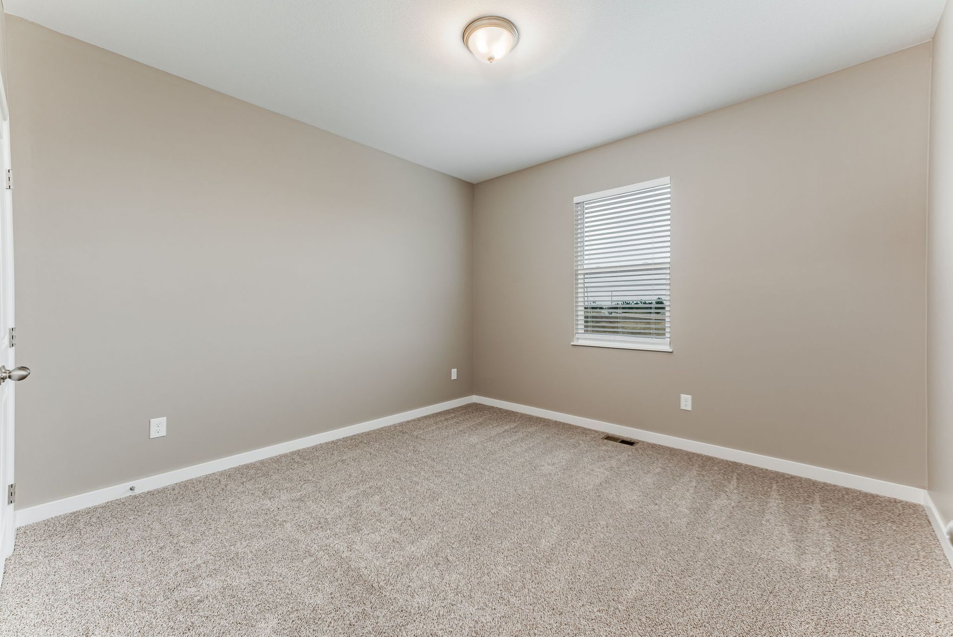 An empty bedroom with a window and a carpeted floor.