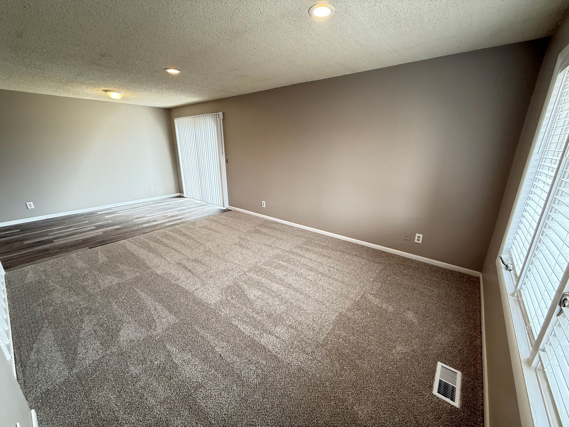 An empty living room with a carpeted floor and brown walls.