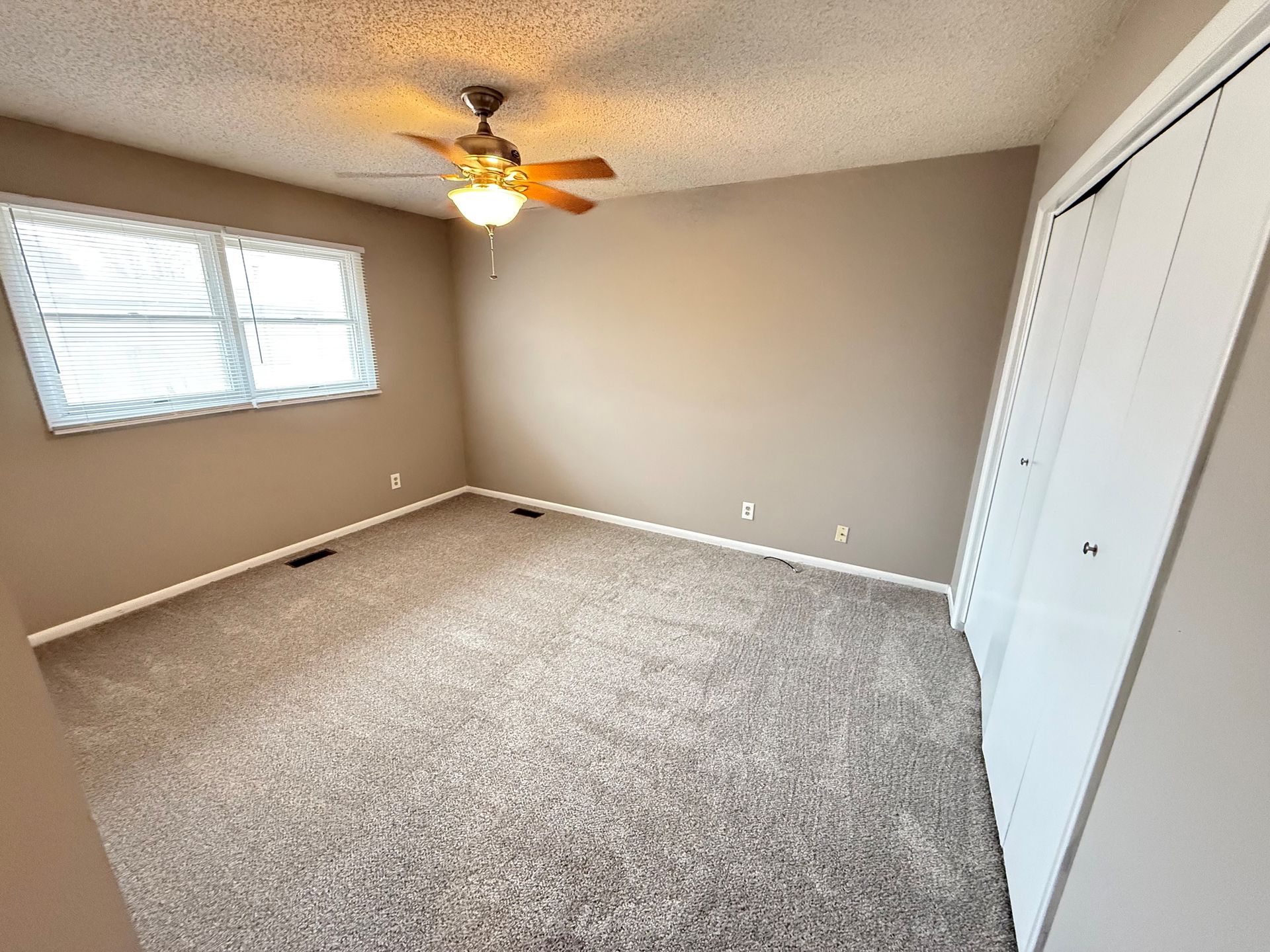 An empty bedroom with a ceiling fan and two windows.