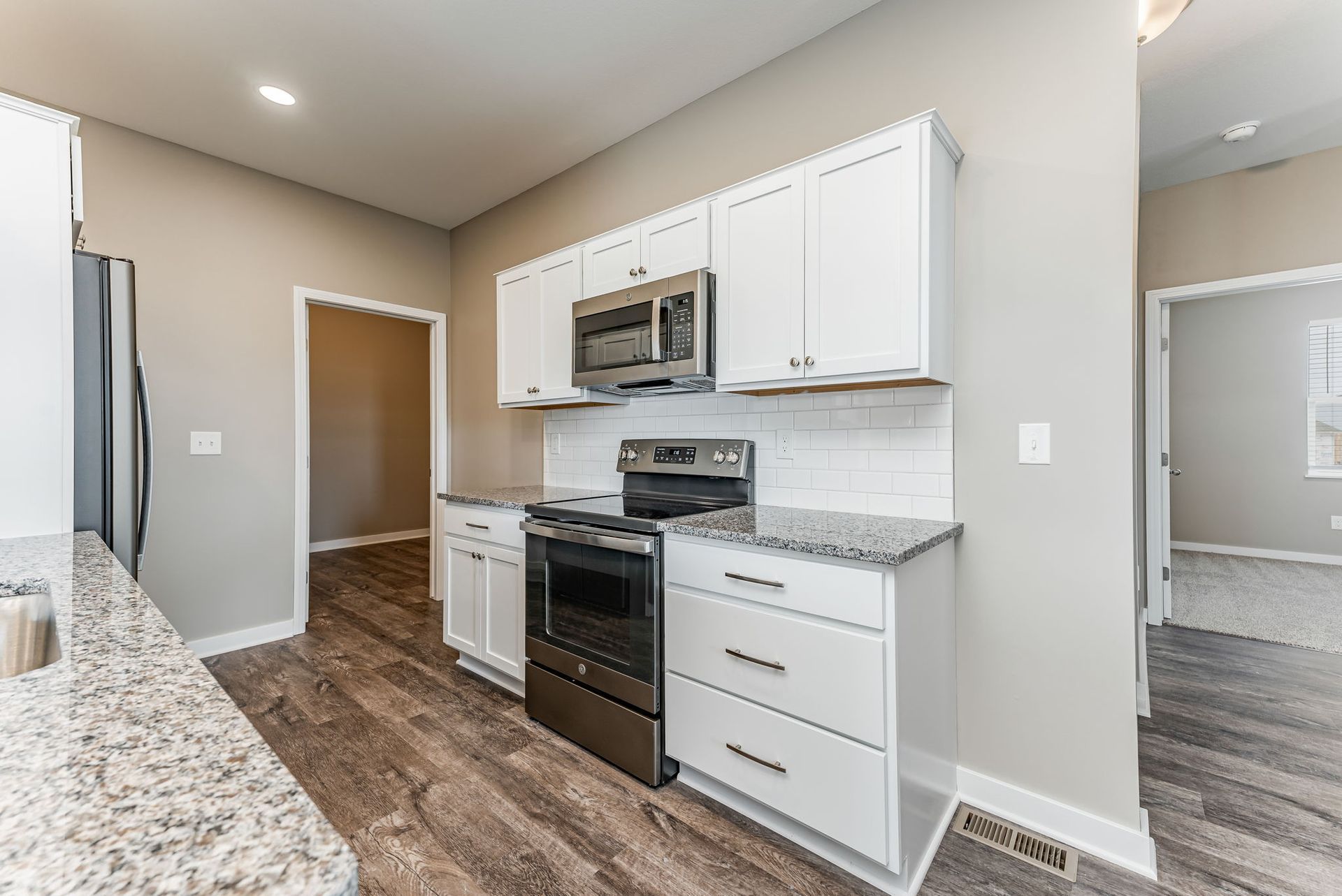 A kitchen with white cabinets , stainless steel appliances , granite counter tops and hardwood floors.