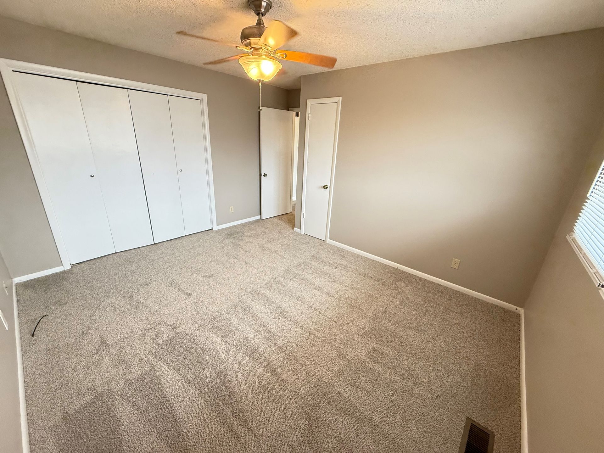 An empty bedroom with a ceiling fan and a large bed.