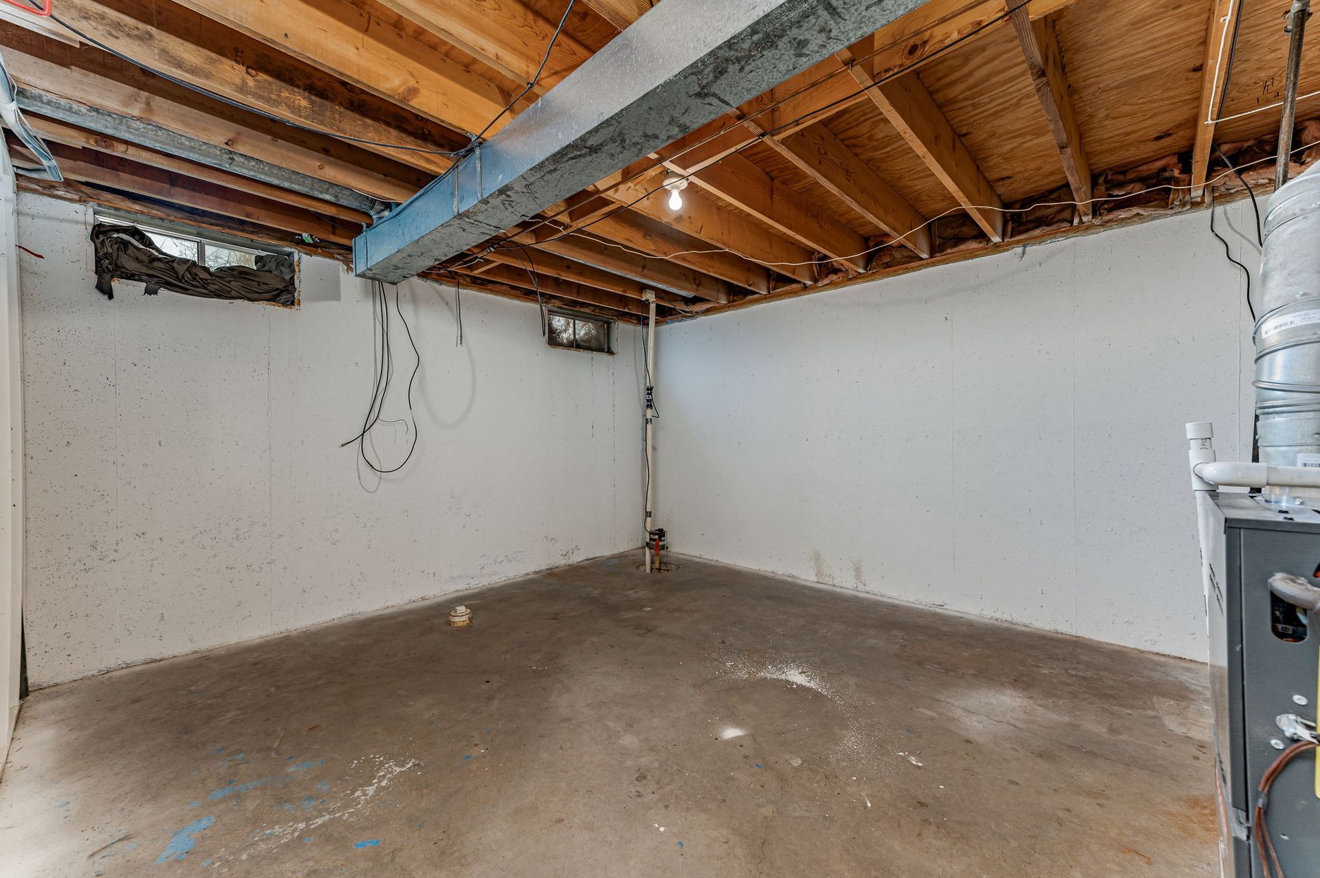 An empty basement with a wooden ceiling and white walls.