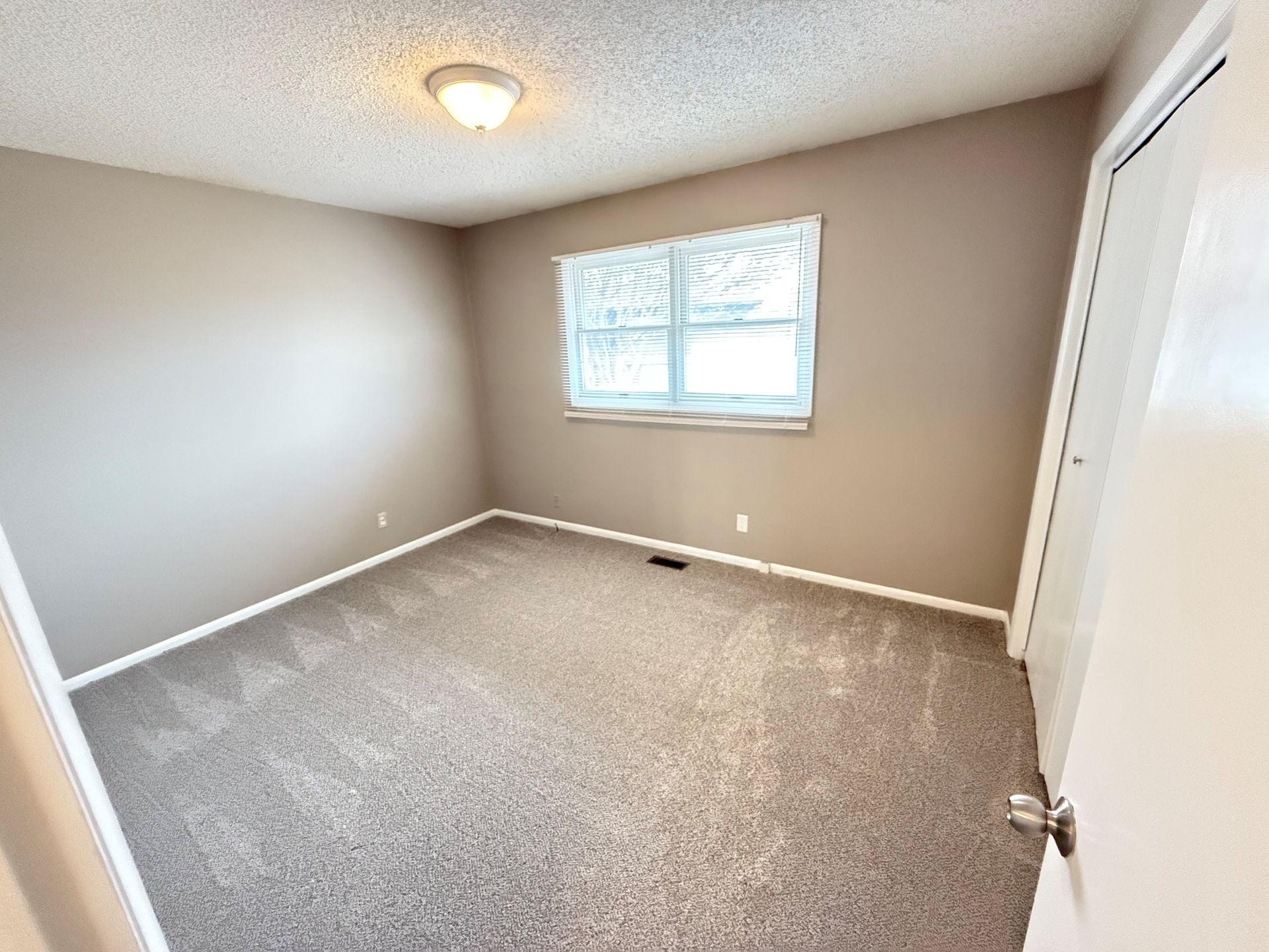 An empty bedroom with a carpeted floor and a window.