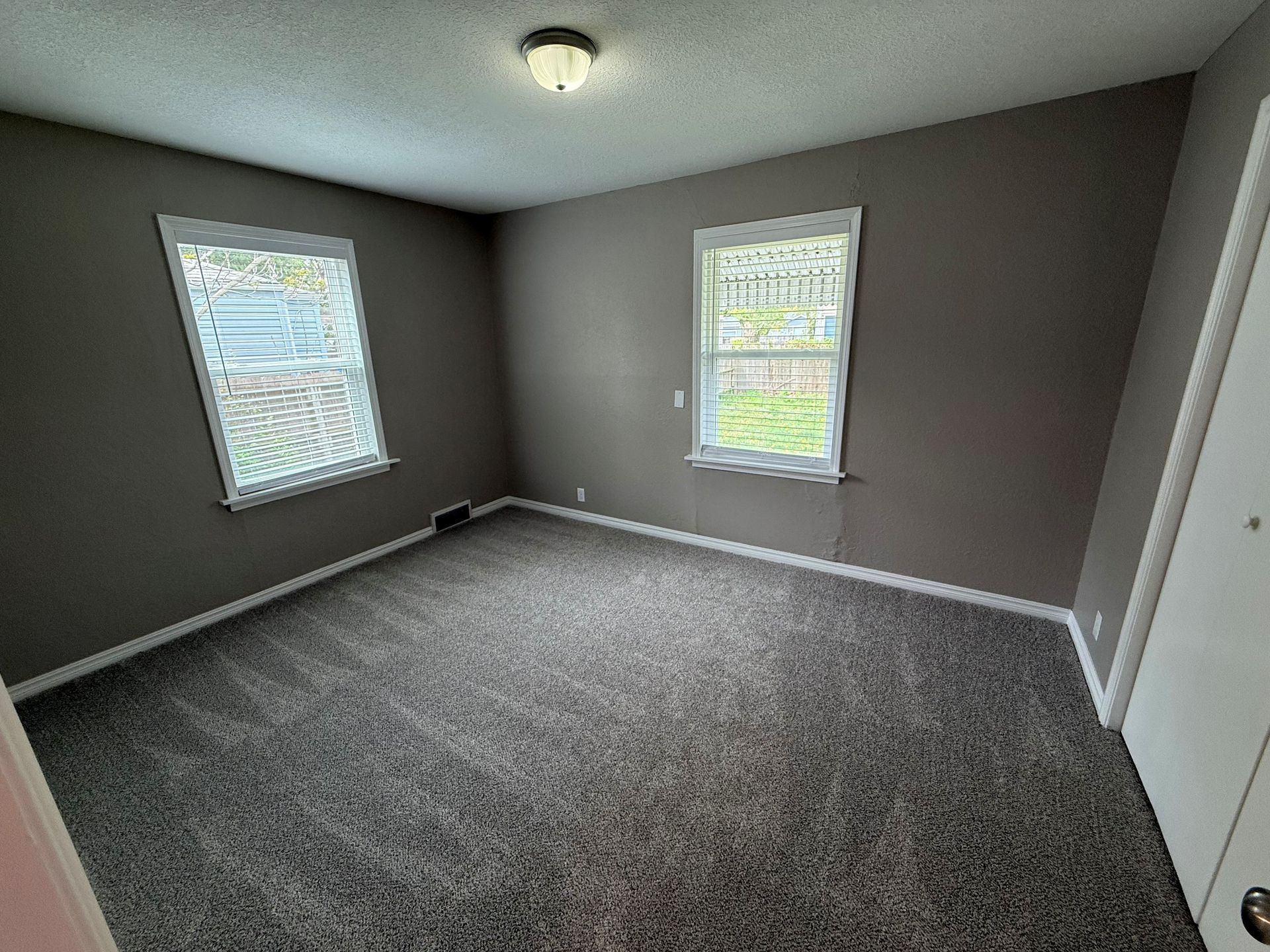 An empty bedroom with a carpeted floor and two windows.