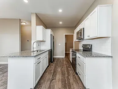 A kitchen with white cabinets , granite counter tops , stainless steel appliances and hardwood floors.