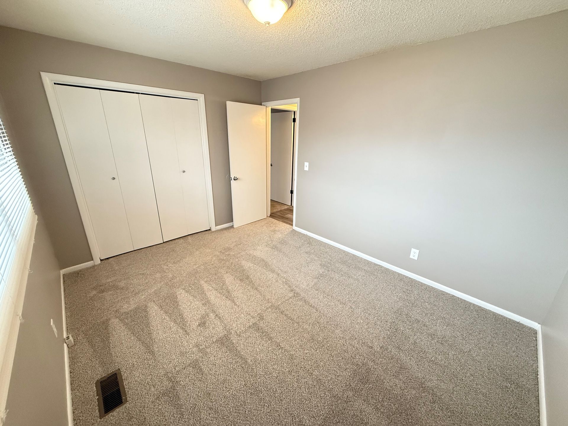 An empty bedroom with a carpeted floor and a closet.