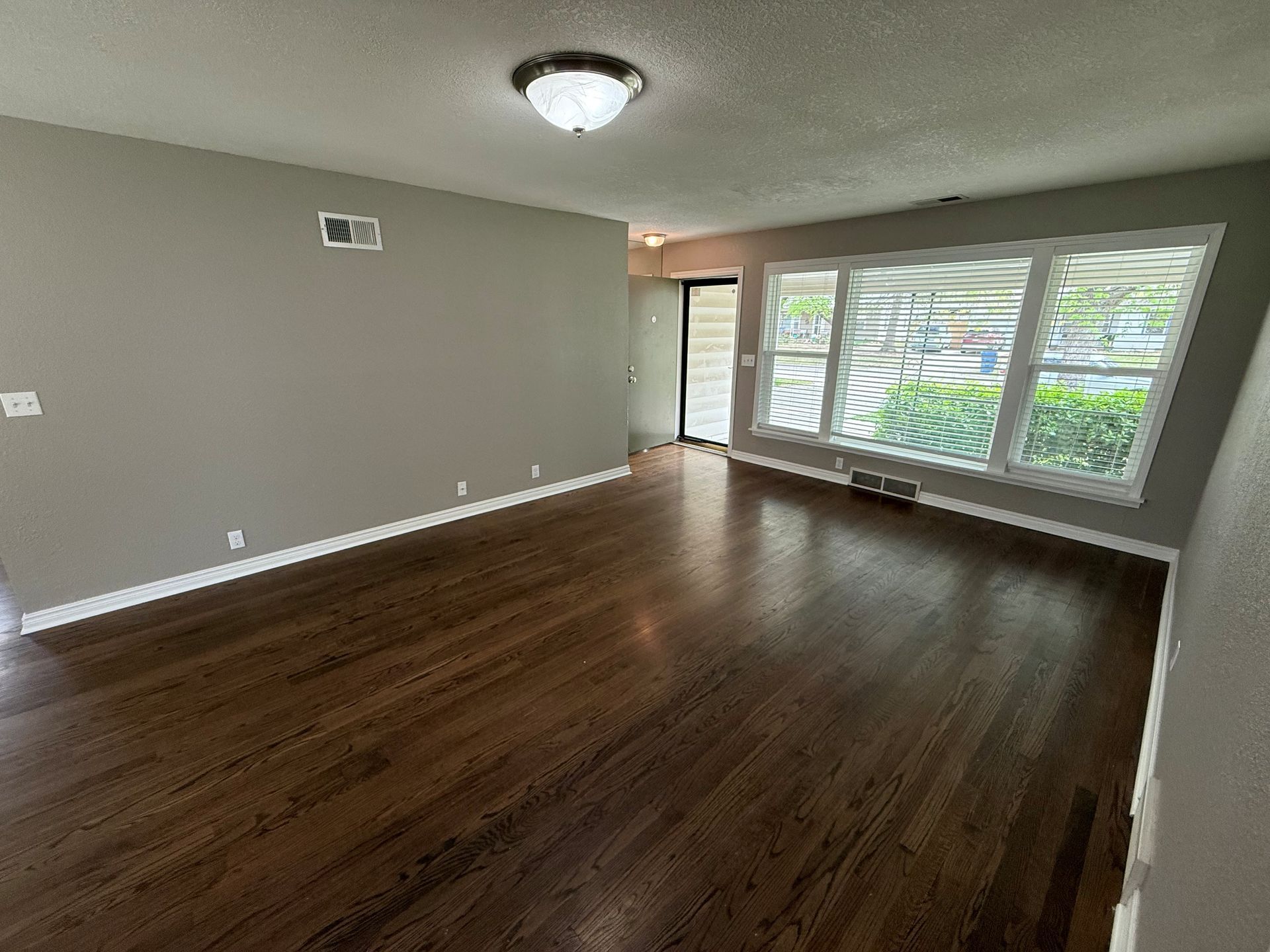 An empty living room with hardwood floors and a lot of windows.