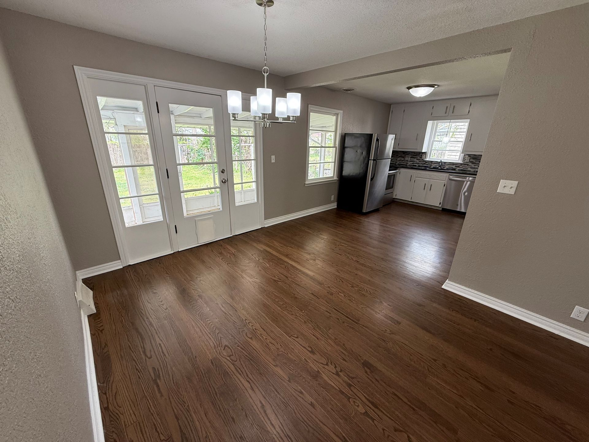 An empty dining room with hardwood floors and a chandelier hanging from the ceiling.