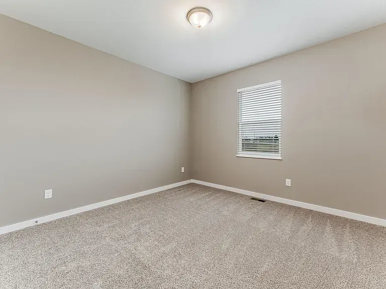 An empty bedroom with a window and a carpeted floor.