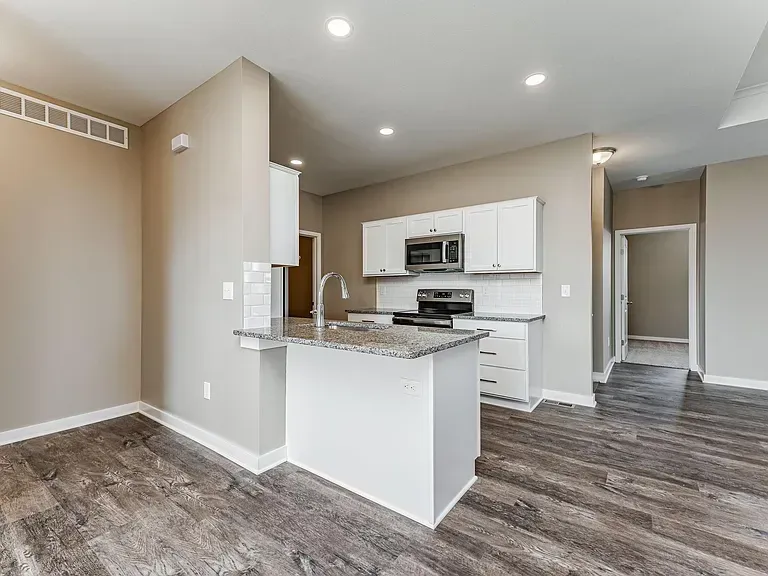 A kitchen with white cabinets , granite counter tops , stainless steel appliances and hardwood floors.