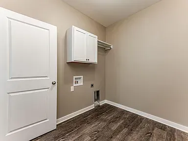 A laundry room with hardwood floors , white cabinets , and a washer and dryer.