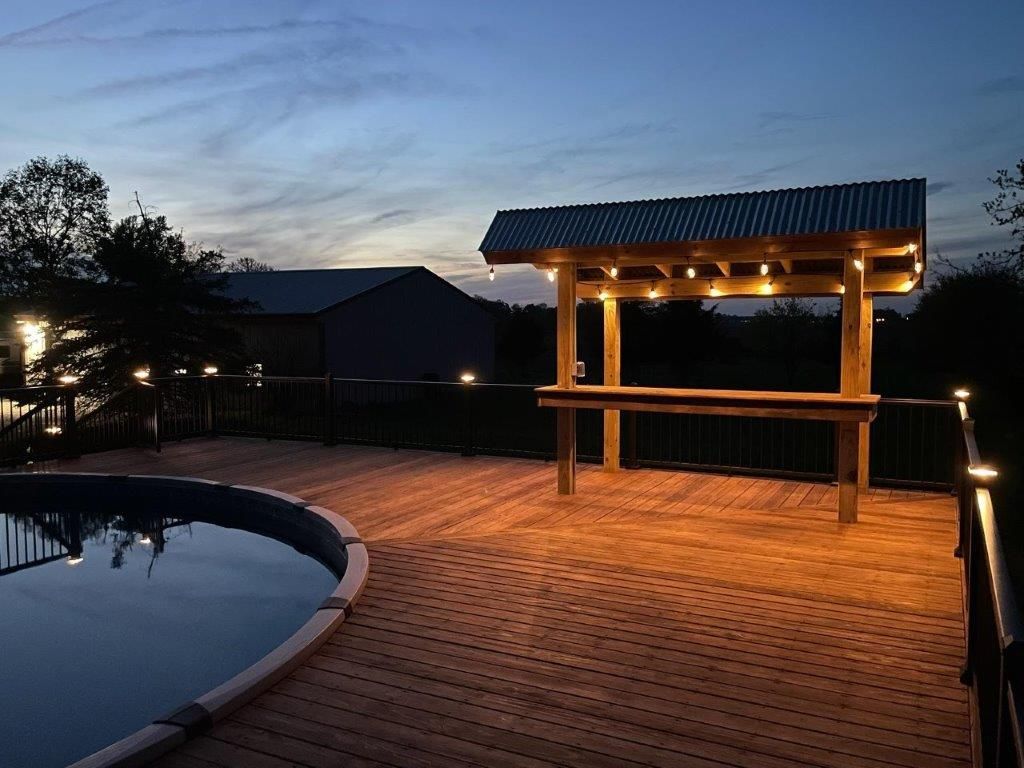 A wooden deck next to a swimming pool at night