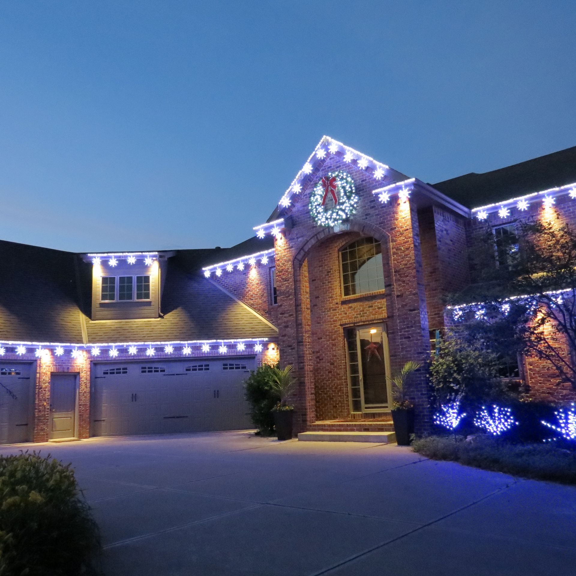 Suburban brick house at dusk, lit with white and blue holiday lights along the roofline and entryway.