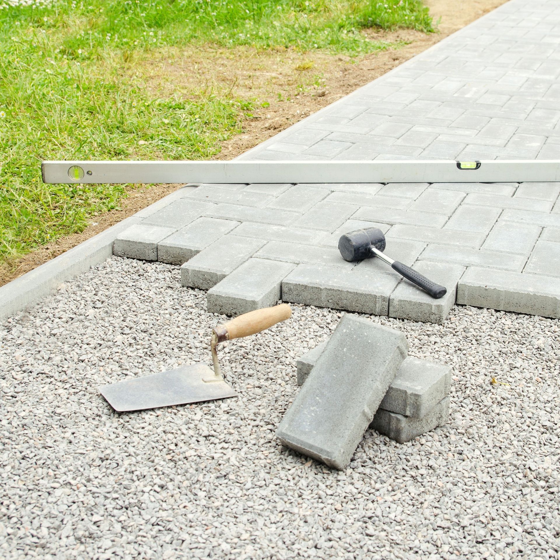 Pavers, a level, a mallet, and a trowel on a gravel base during a sidewalk construction project.