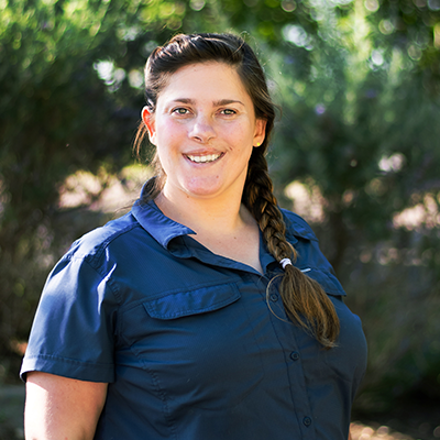 Woman smiling outdoors, wearing a dark blue shirt with her hair in a braid.