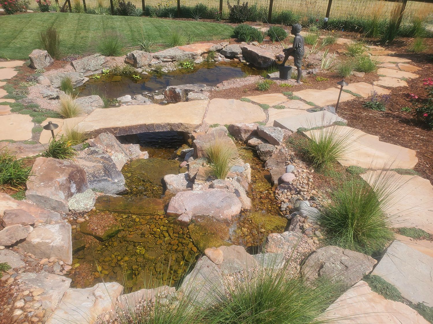 A stone-lined garden pond and stream feature with surrounding flagstone paths and landscaping.