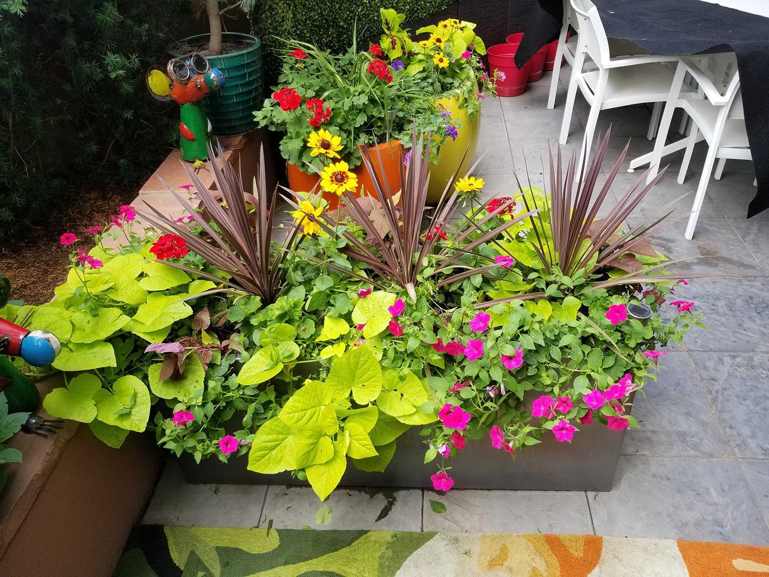 A rectangular planter filled with vibrant flowers and foliage, including purple grasses and bright green leaves, on a patio.