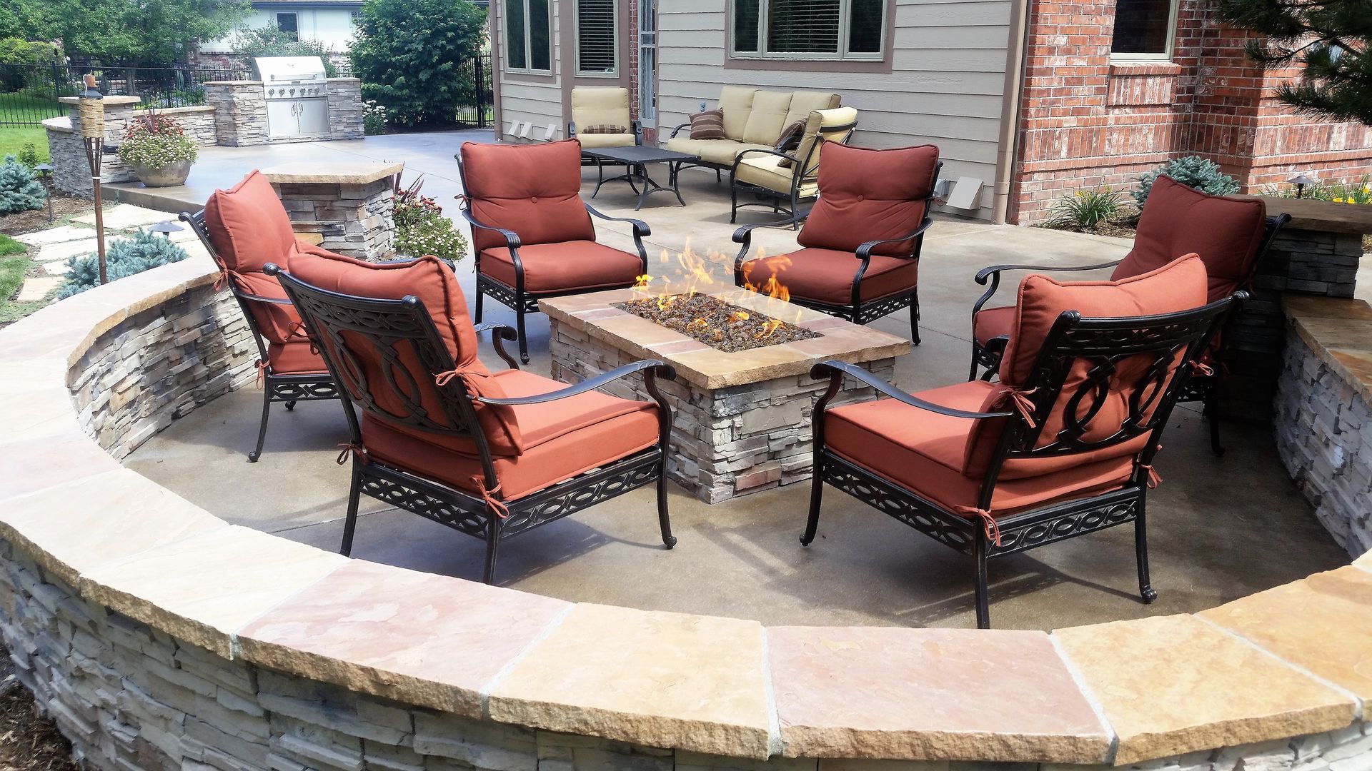 Outdoor patio with fire pit and seating, surrounded by stone walls.