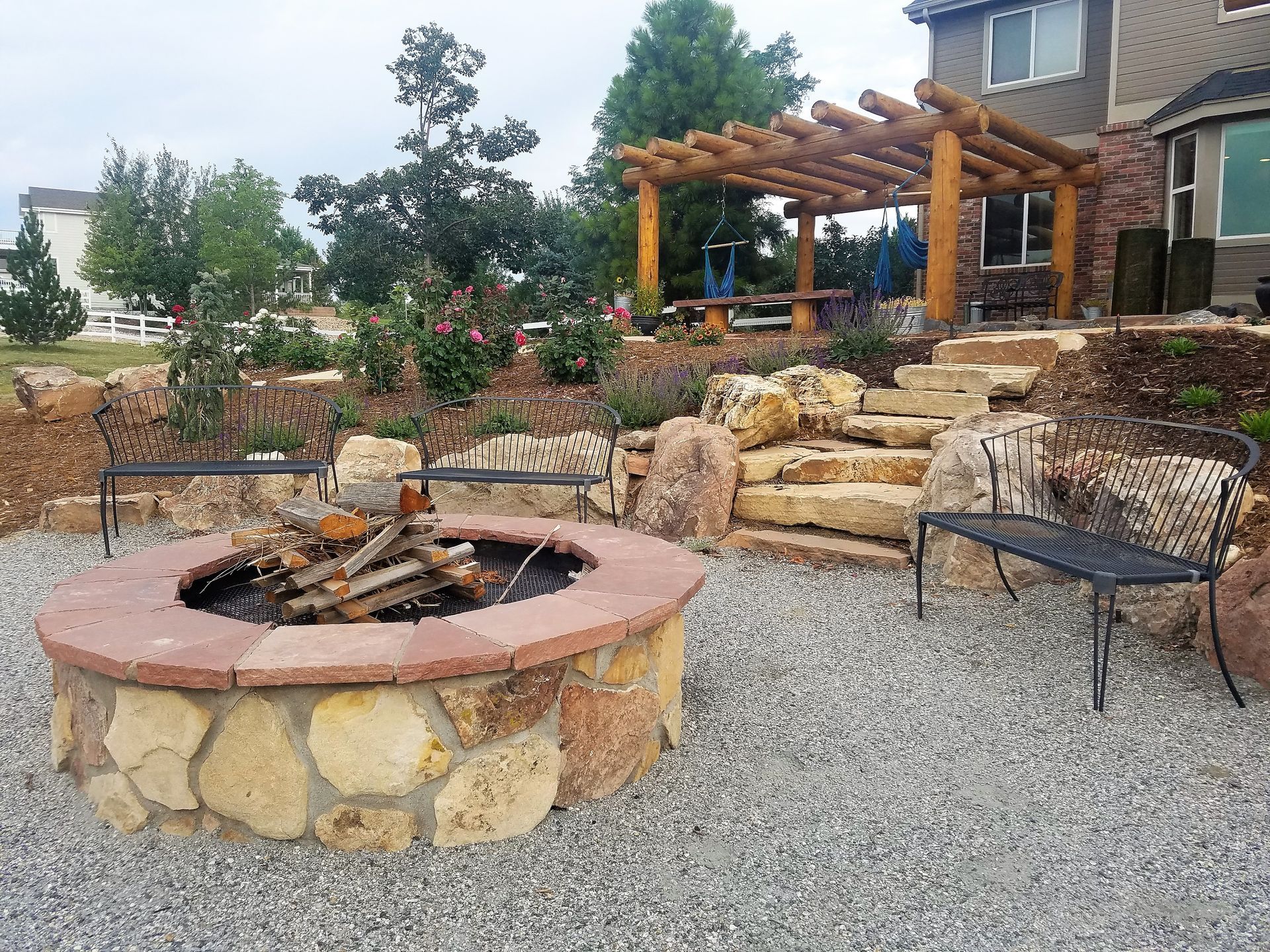 Stone fire pit with benches in a backyard patio with a pergola and steps.