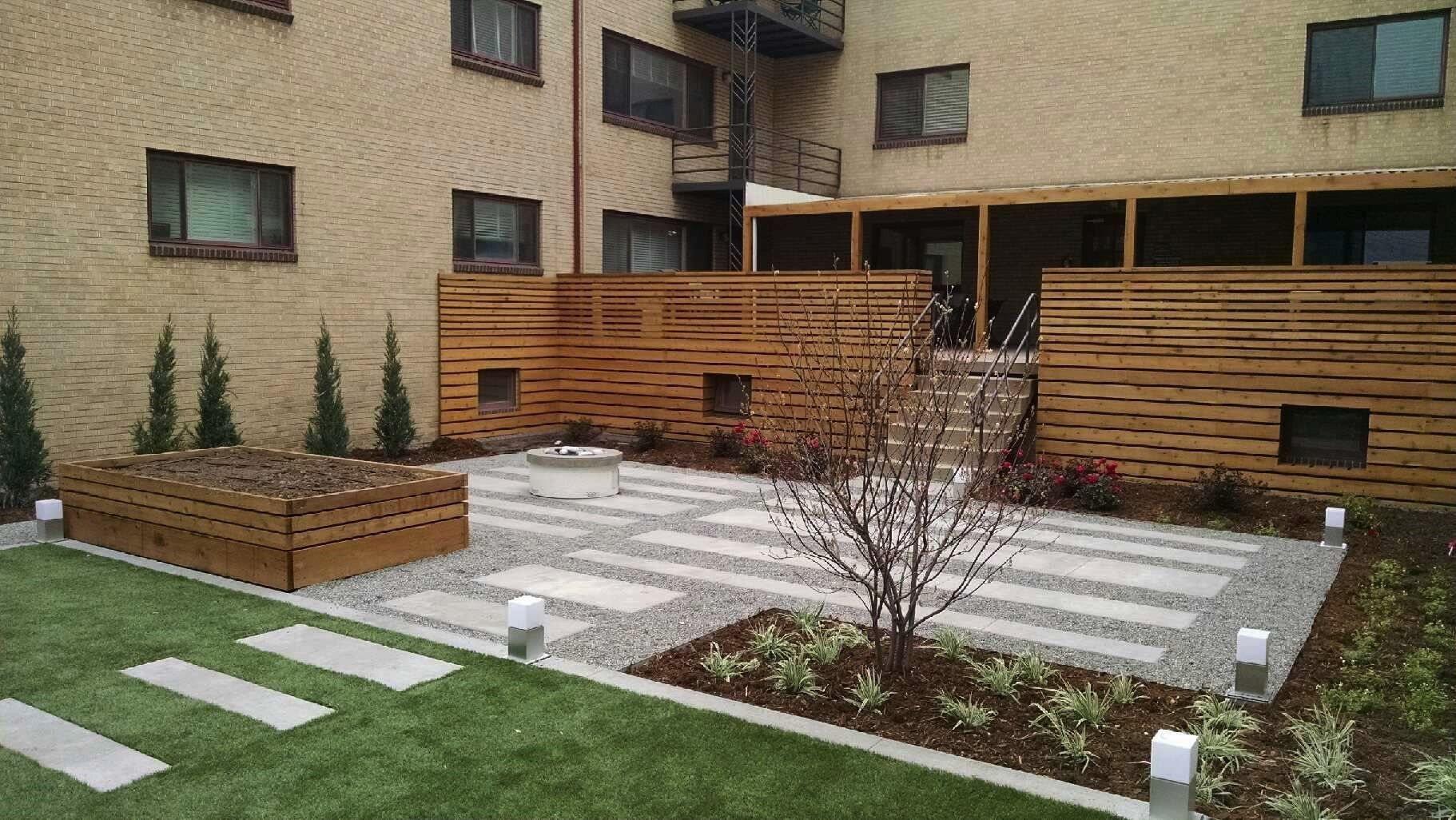 Backyard patio with wooden fence, stepping stones, small trees, and a building in the background.