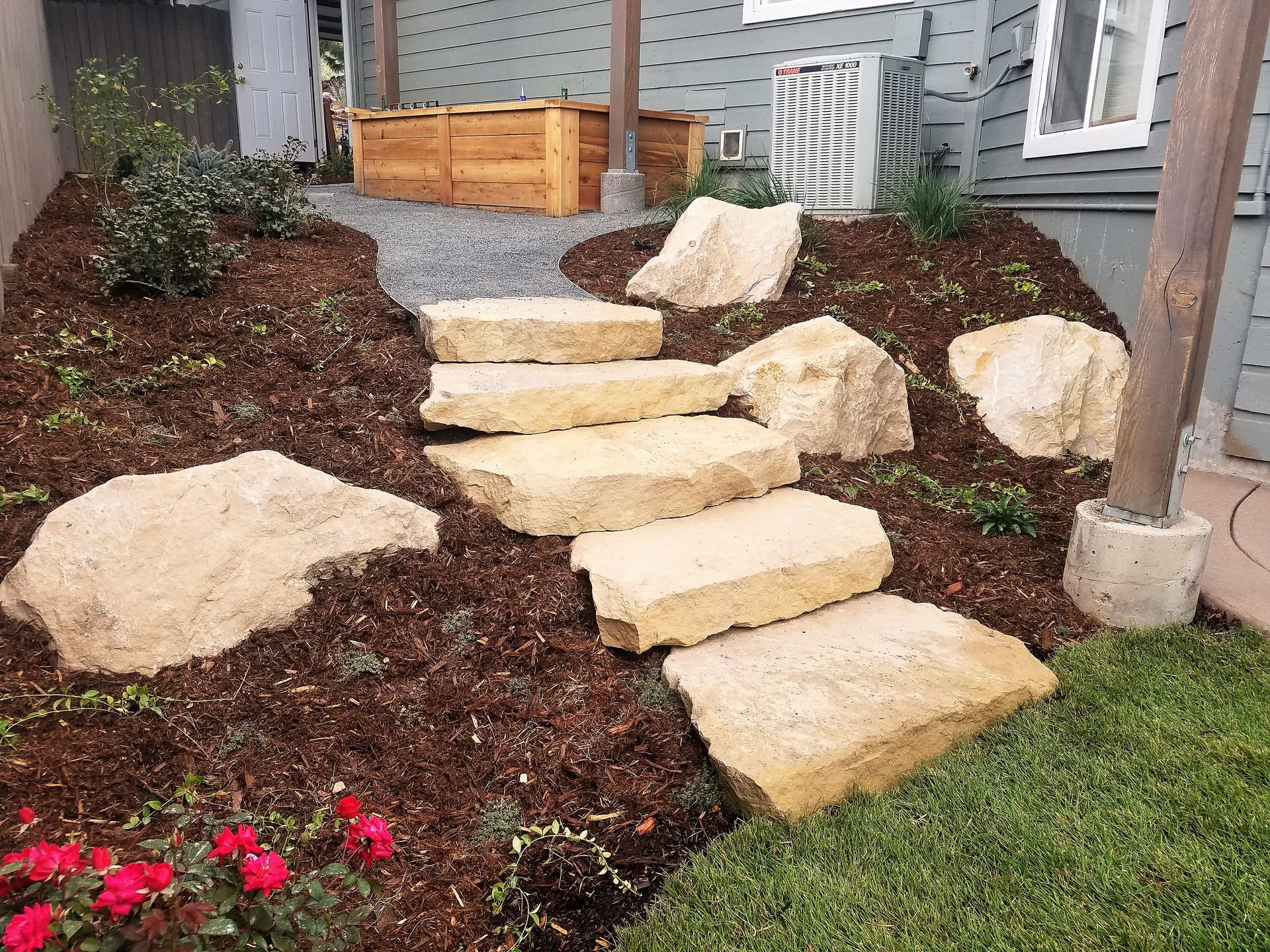 Stone steps lead up a mulched slope in a garden, with greenery and a wooden planter box.