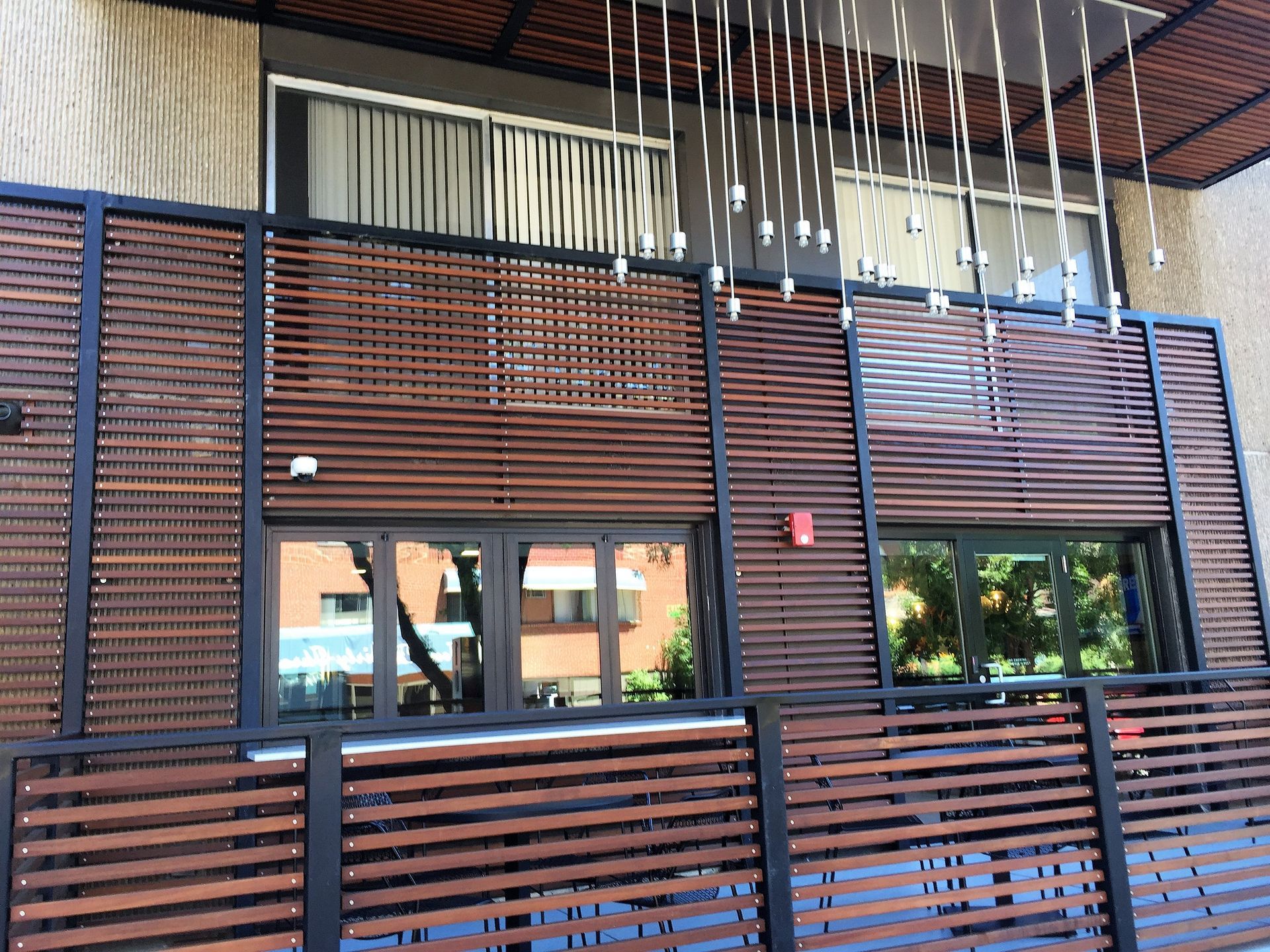 Exterior of a building with brown horizontal wooden slats, dark framed windows, and a modern light fixture.