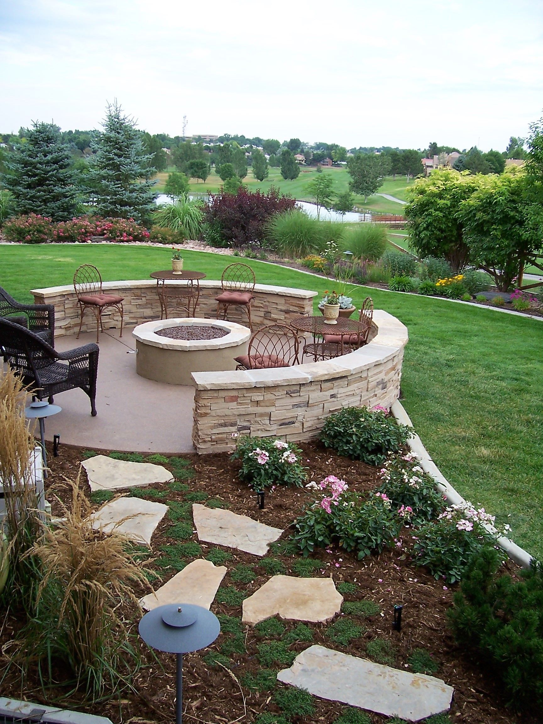 Stone fire pit with seating in a landscaped yard overlooking a golf course.