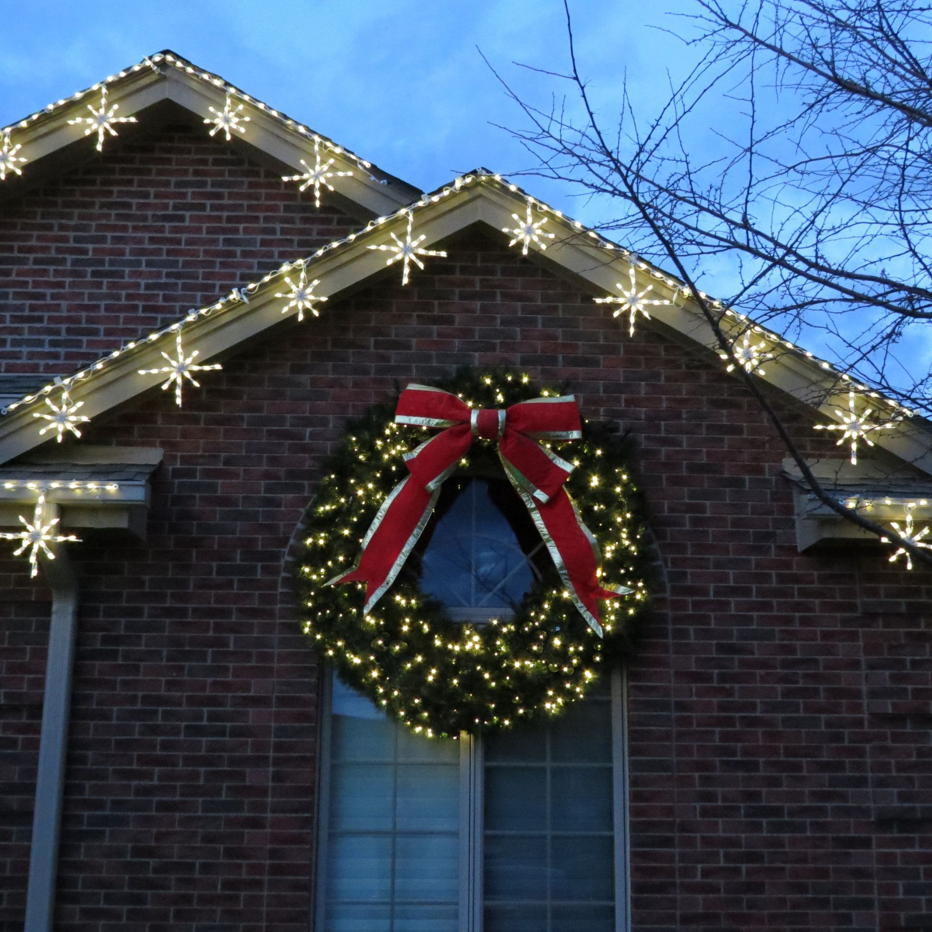 Brick house with Christmas lights and a wreath with a red bow.