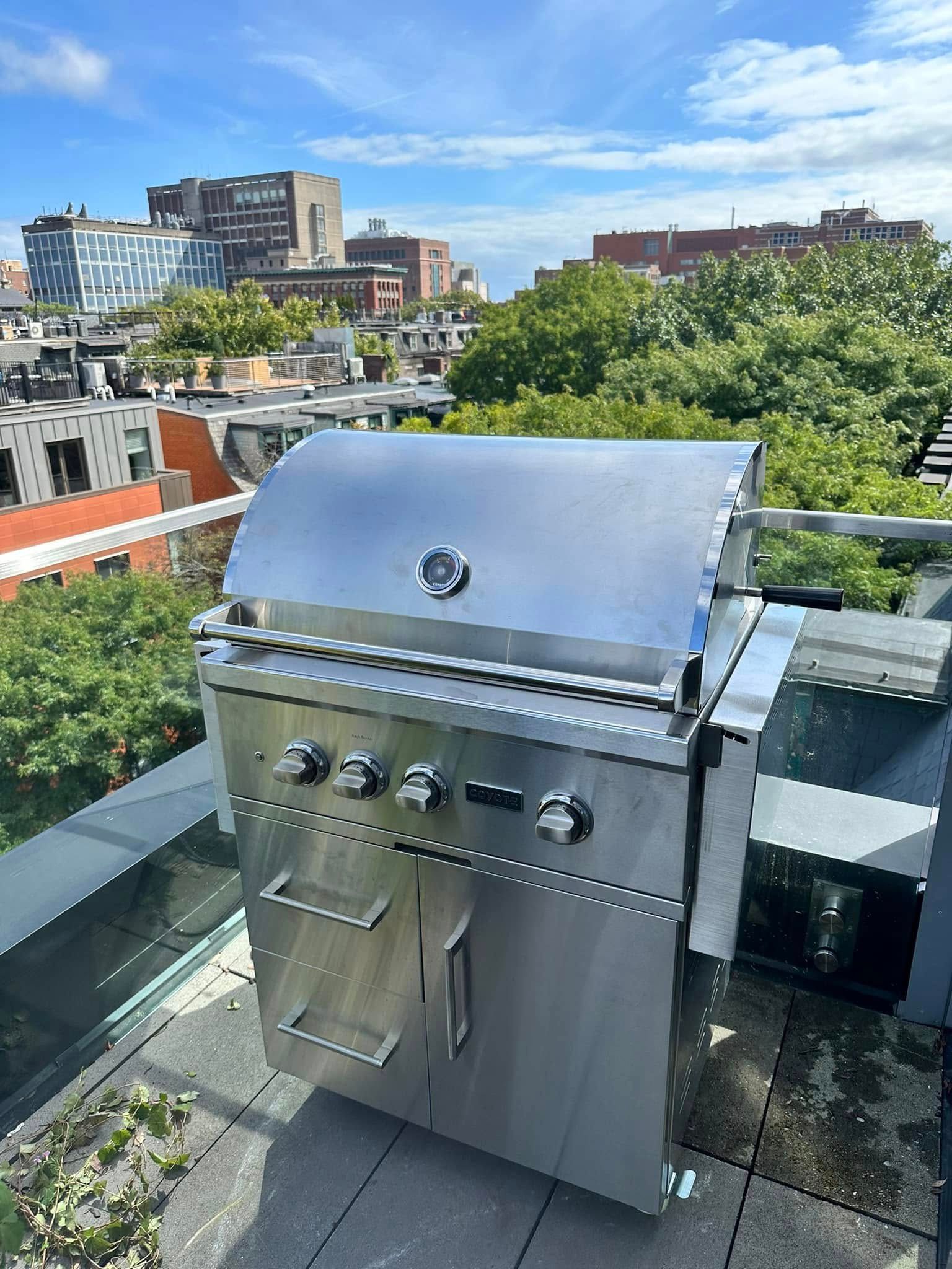 A stainless steel grill is sitting on a balcony overlooking a city.