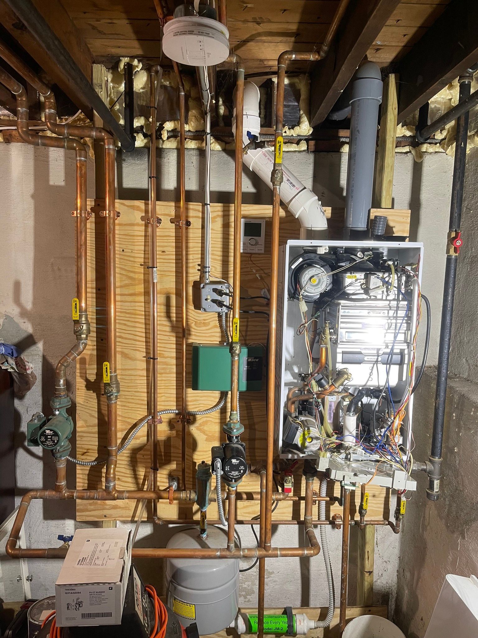 A boiler is sitting in a basement surrounded by pipes.