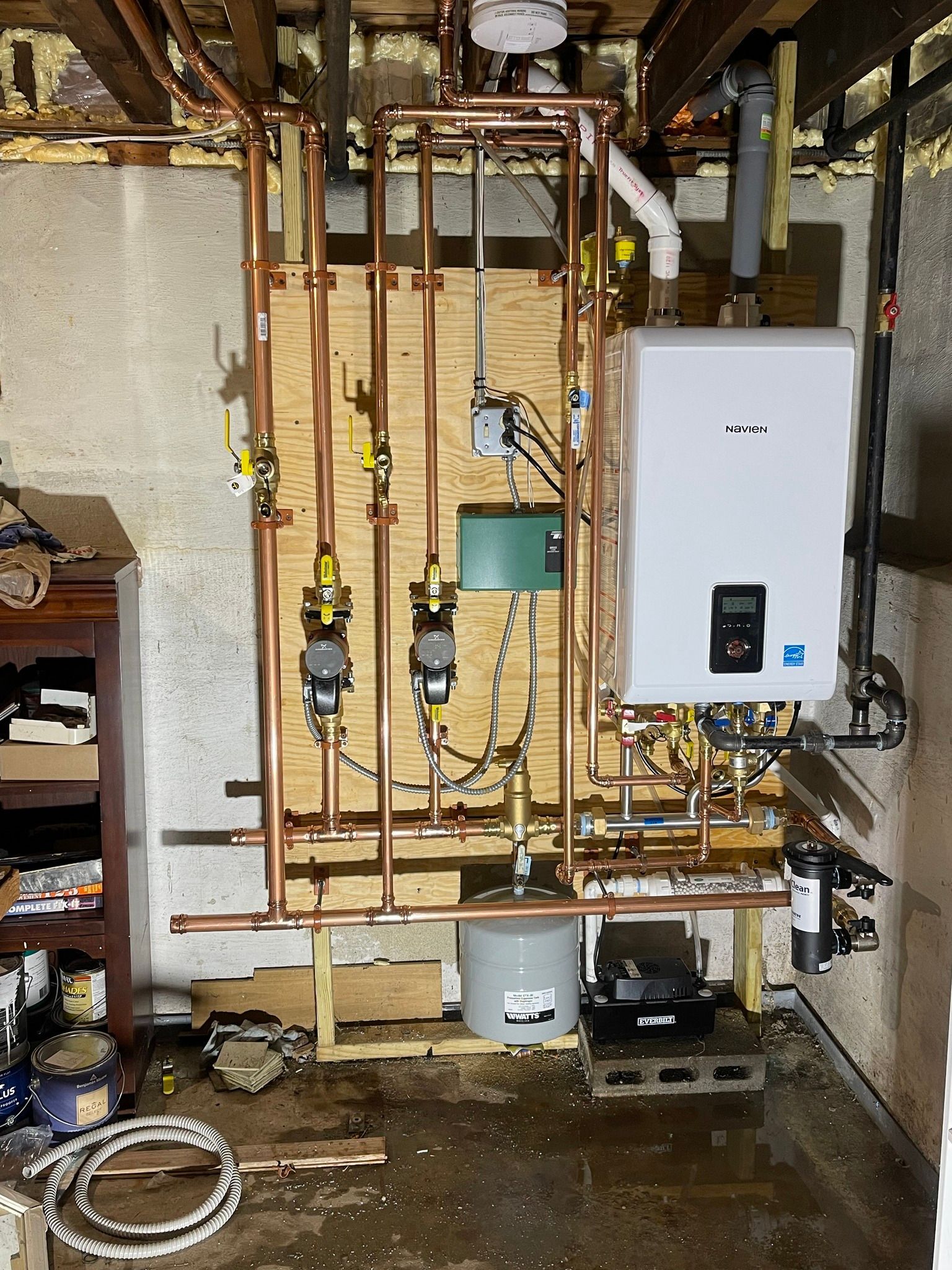 A room with a lot of pipes and a boiler on the wall.