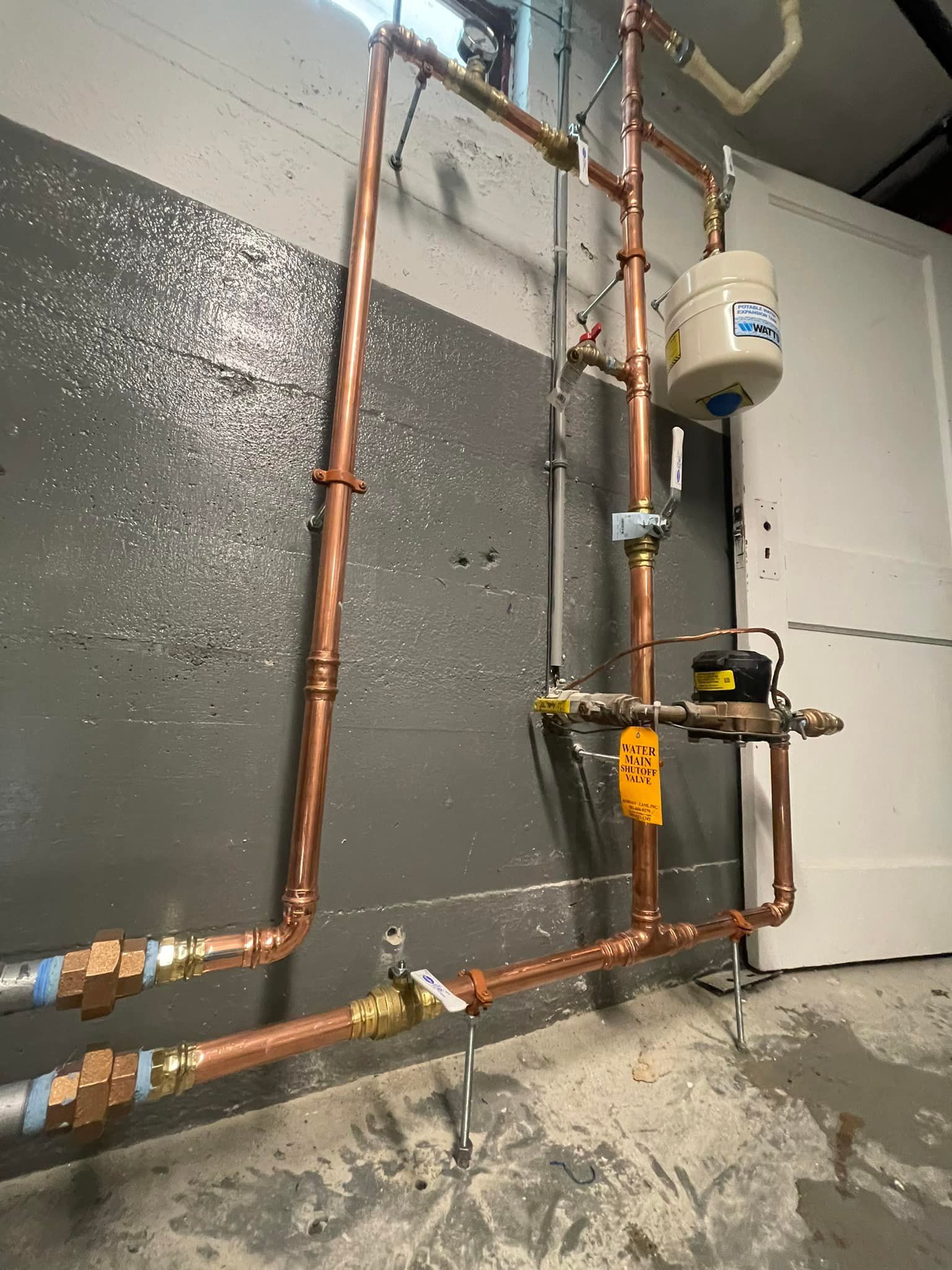 A room with copper pipes and a water heater on the wall.