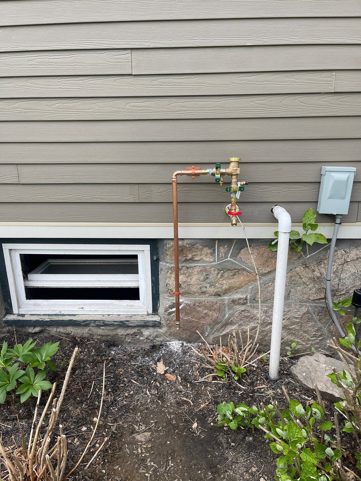 A hose is attached to the side of a house next to a window.